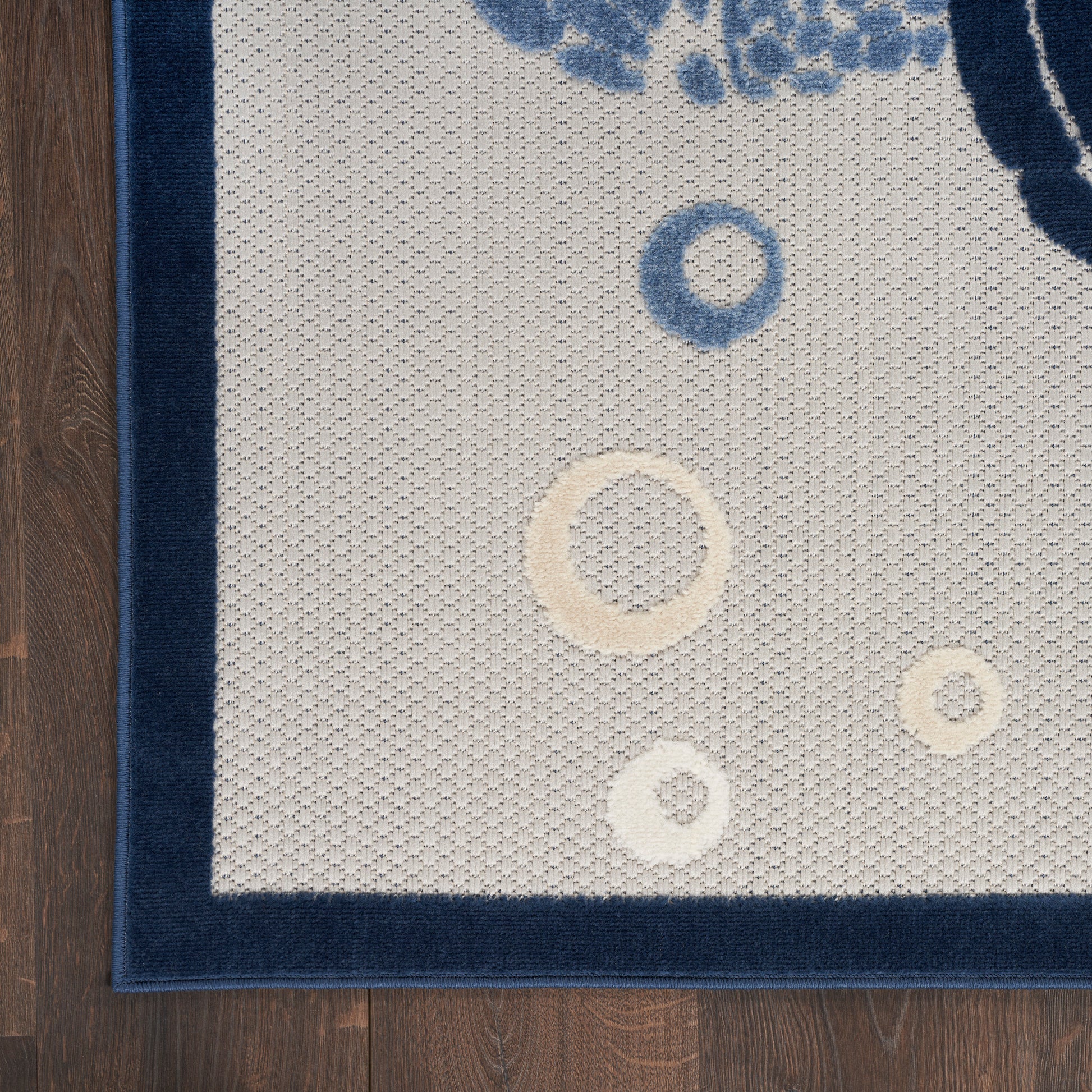 Rectangular beige loop-pile rug with a navy border and blue/cream circular motifs, laid on wood floor.