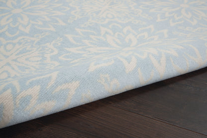 Pale blue rug with white damask floral pattern on dark wood floor.