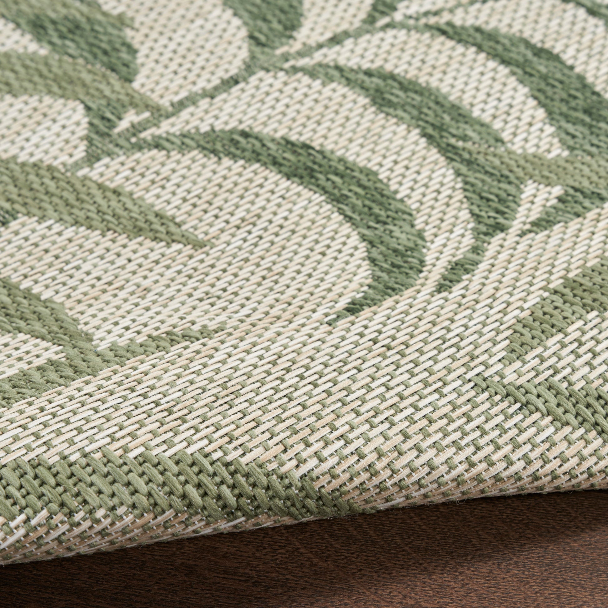 Beige and sage green woven rug with botanical leaf pattern and green border.