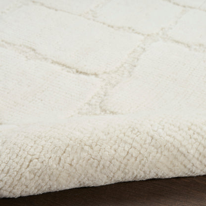 Cream plush rug close-up with thick pile and subtle grid pattern; edge folded on dark wood floor.