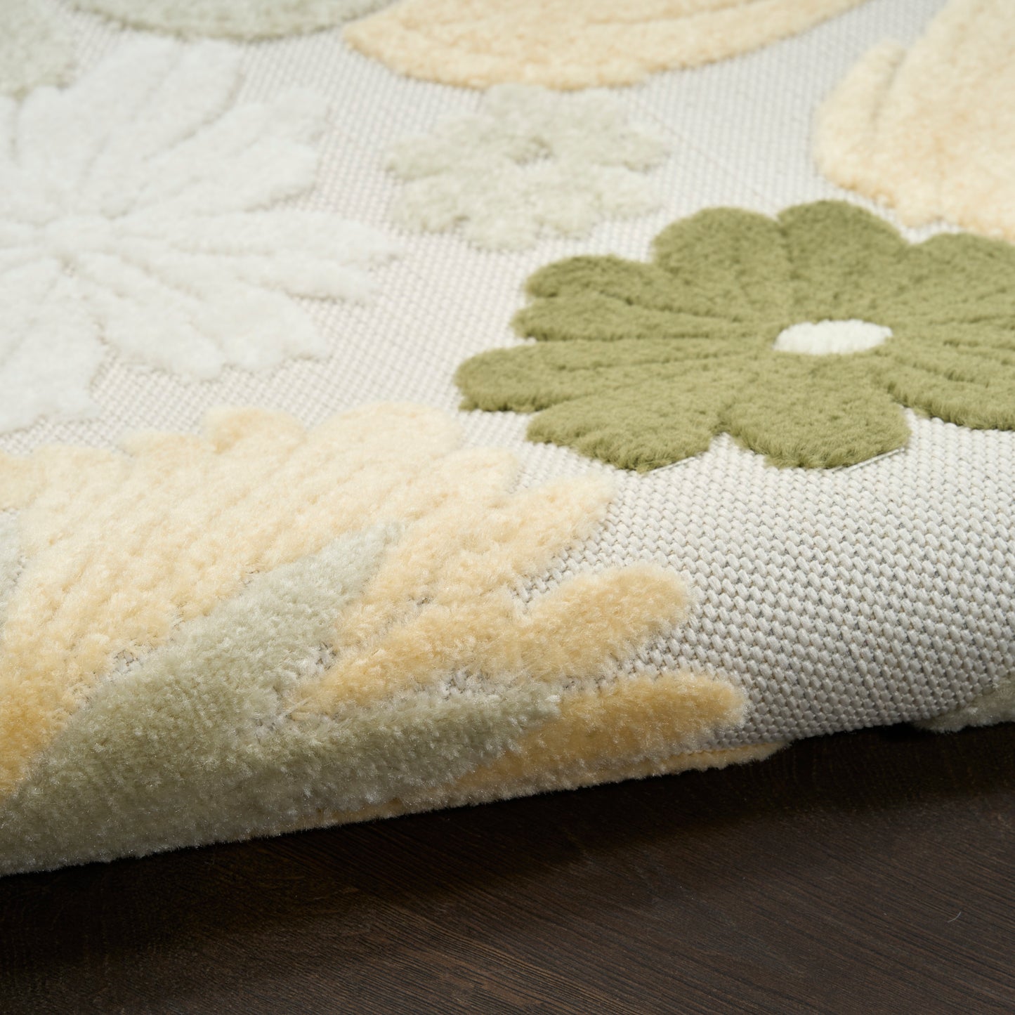Textured floral area rug close-up: cream, olive green and pale yellow plush flowers on a light beige woven base.