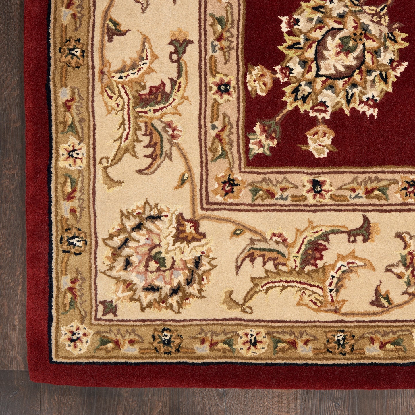 Rectangular oriental rug with cream border and burgundy field; ornate floral vine pattern on a dark wood floor.