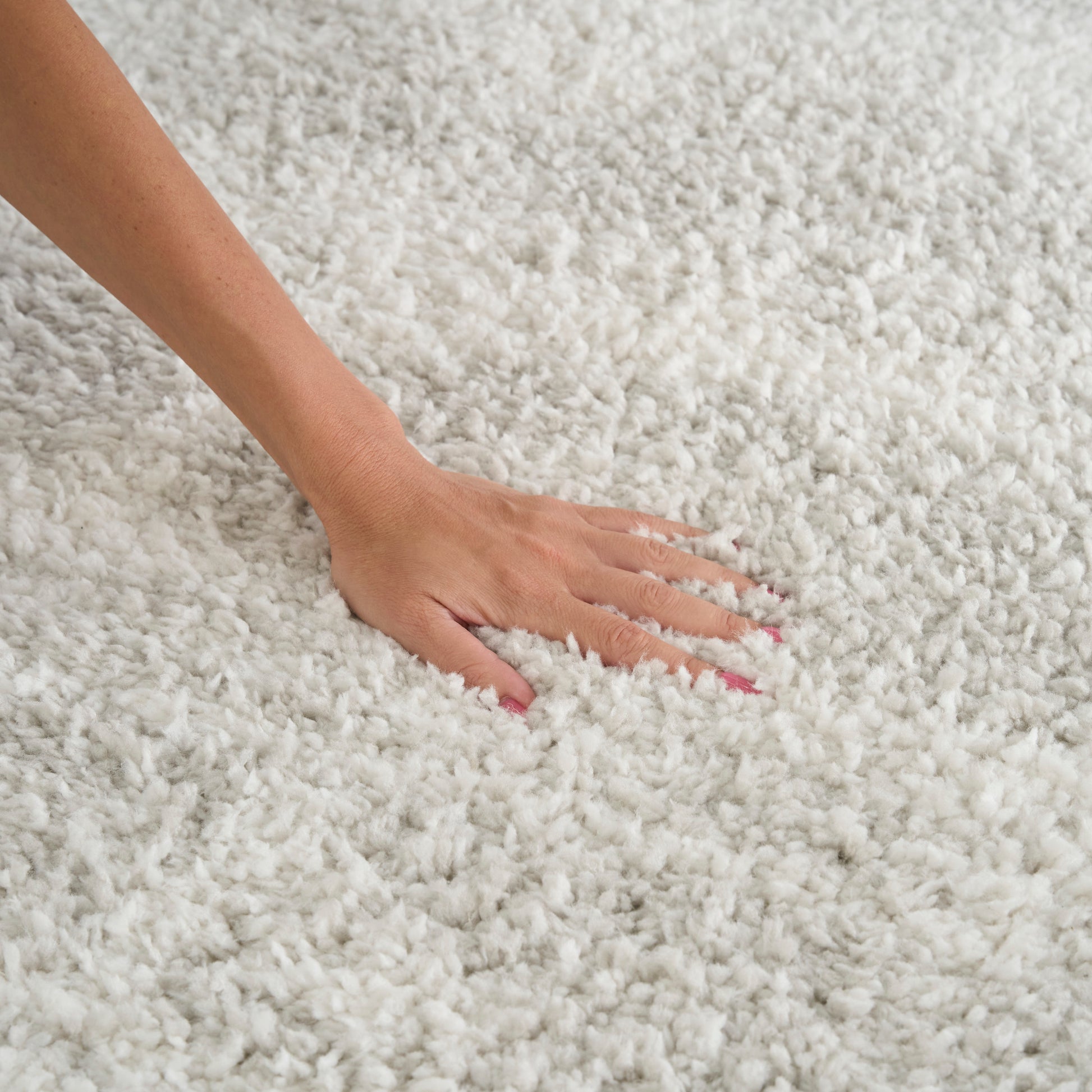 Hand pressing into fluffy ivory shag rug; soft, high-pile cream rug with plush texture.