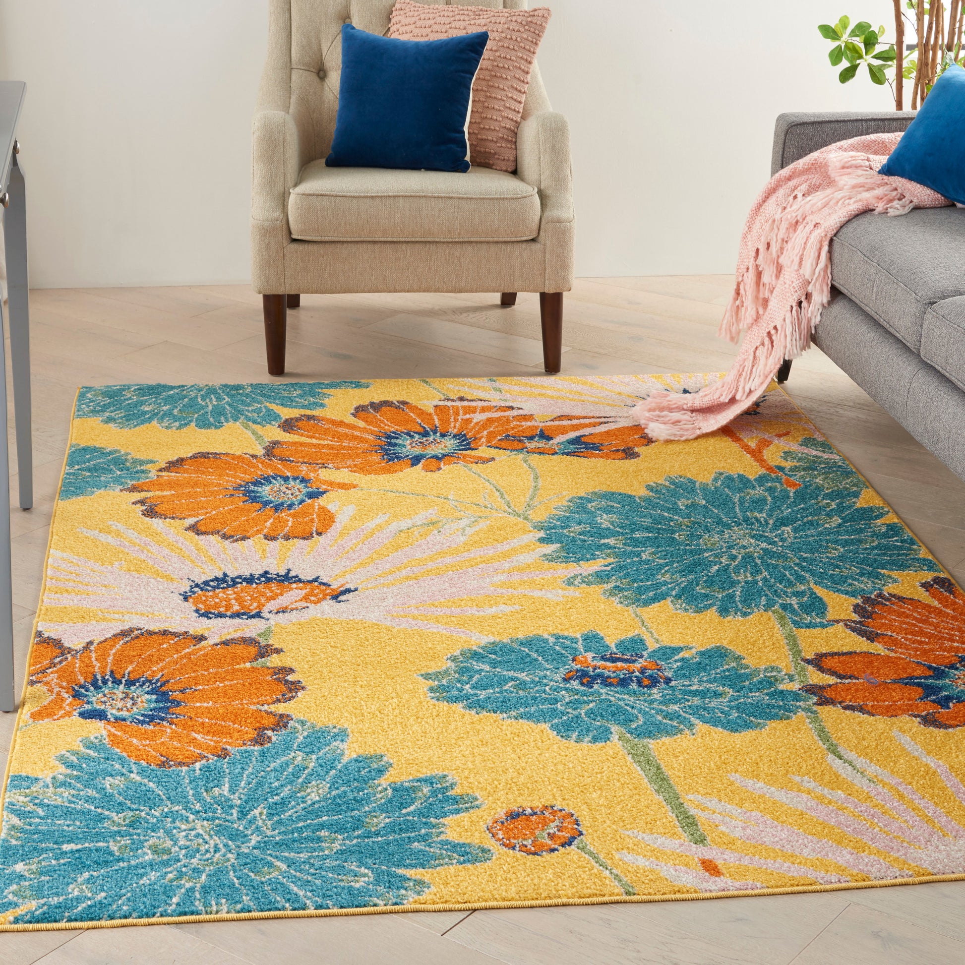 Bright floral area rug with orange and teal flowers on yellow; contemporary living room with beige armchair, pink throw.