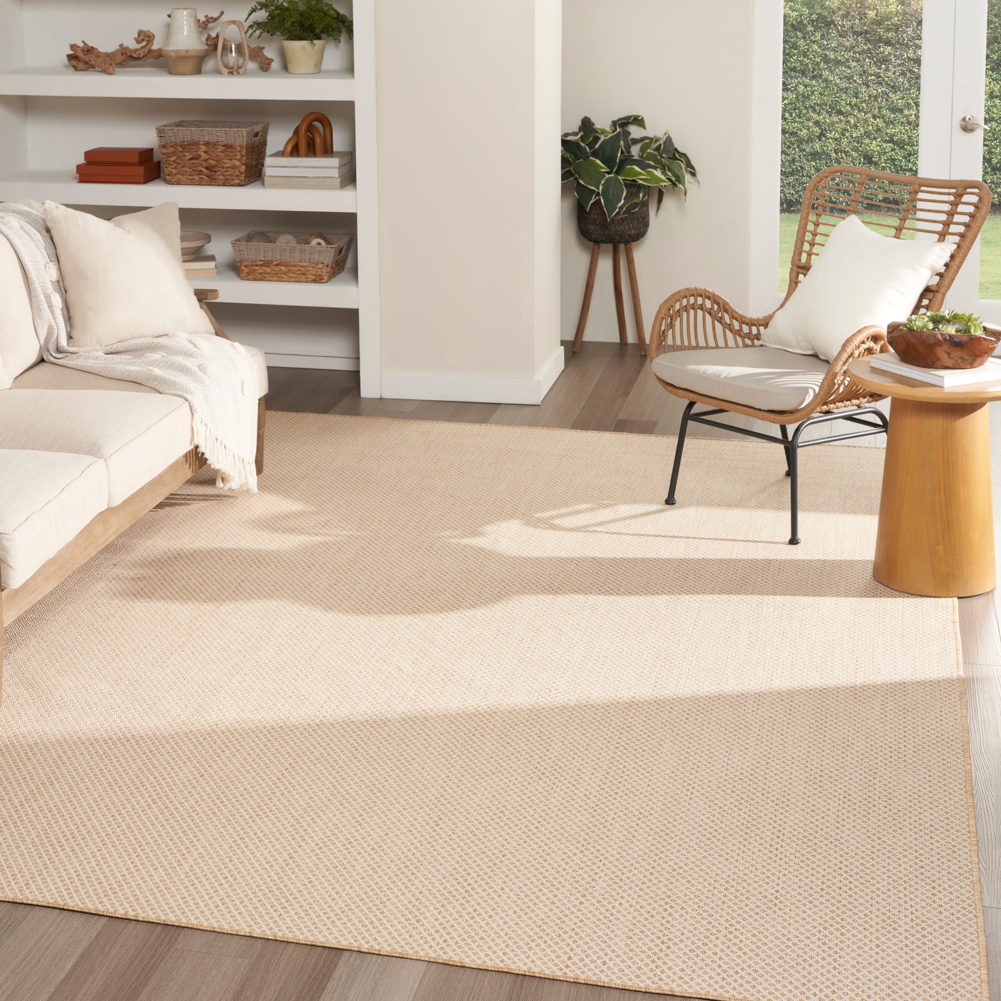Neutral living room with a large beige rug, white sofa, wicker chair, round wood side table and potted plant.