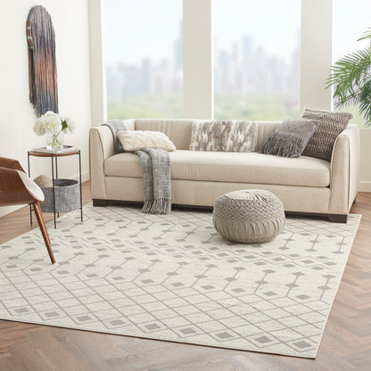 Neutral living room with beige fabric sofa, knitted pouf, geometric gray rug, layered throws, and a wooden chair.