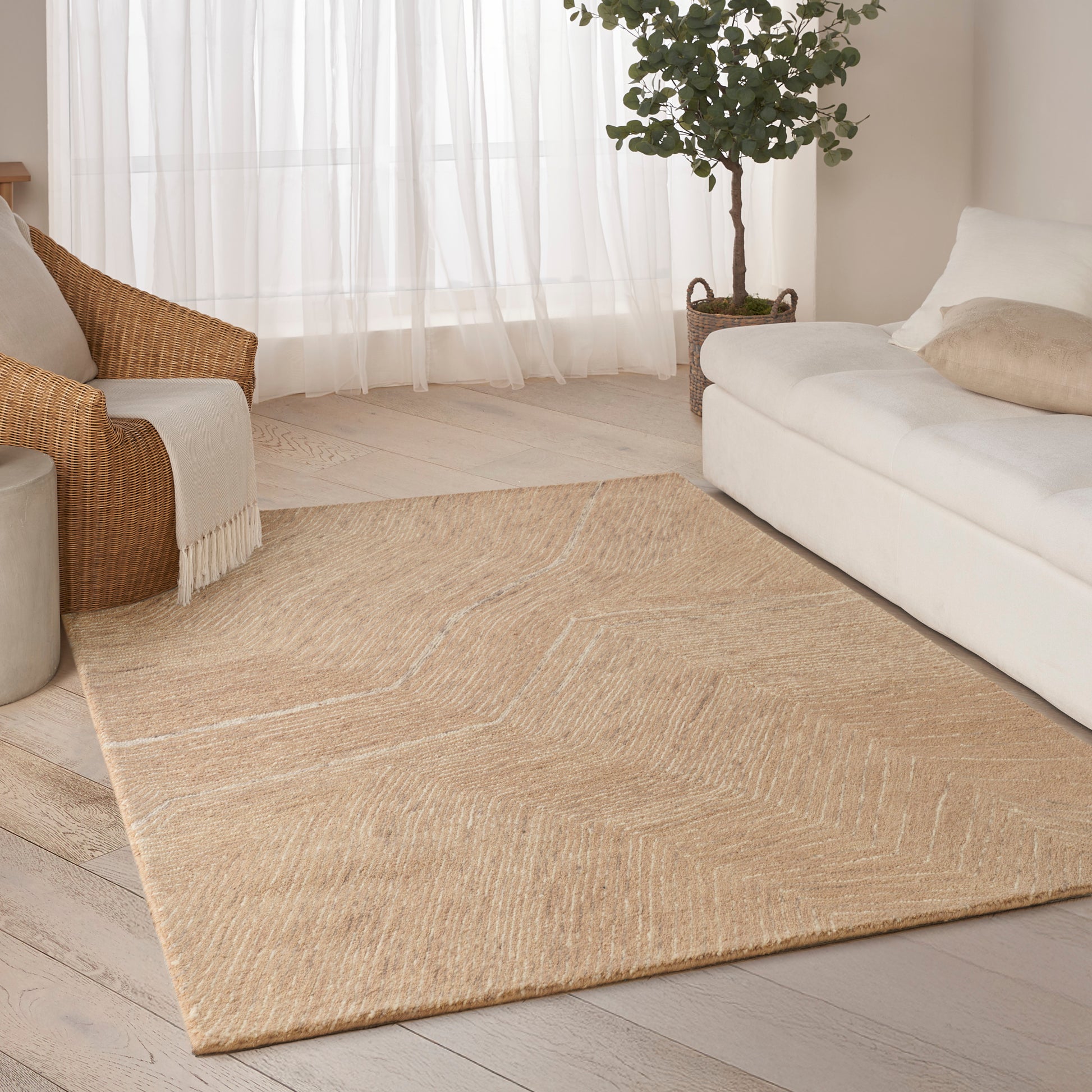 Natural beige jute rug with subtle chevron pattern in a bright living room beside a white sofa and wicker chair.