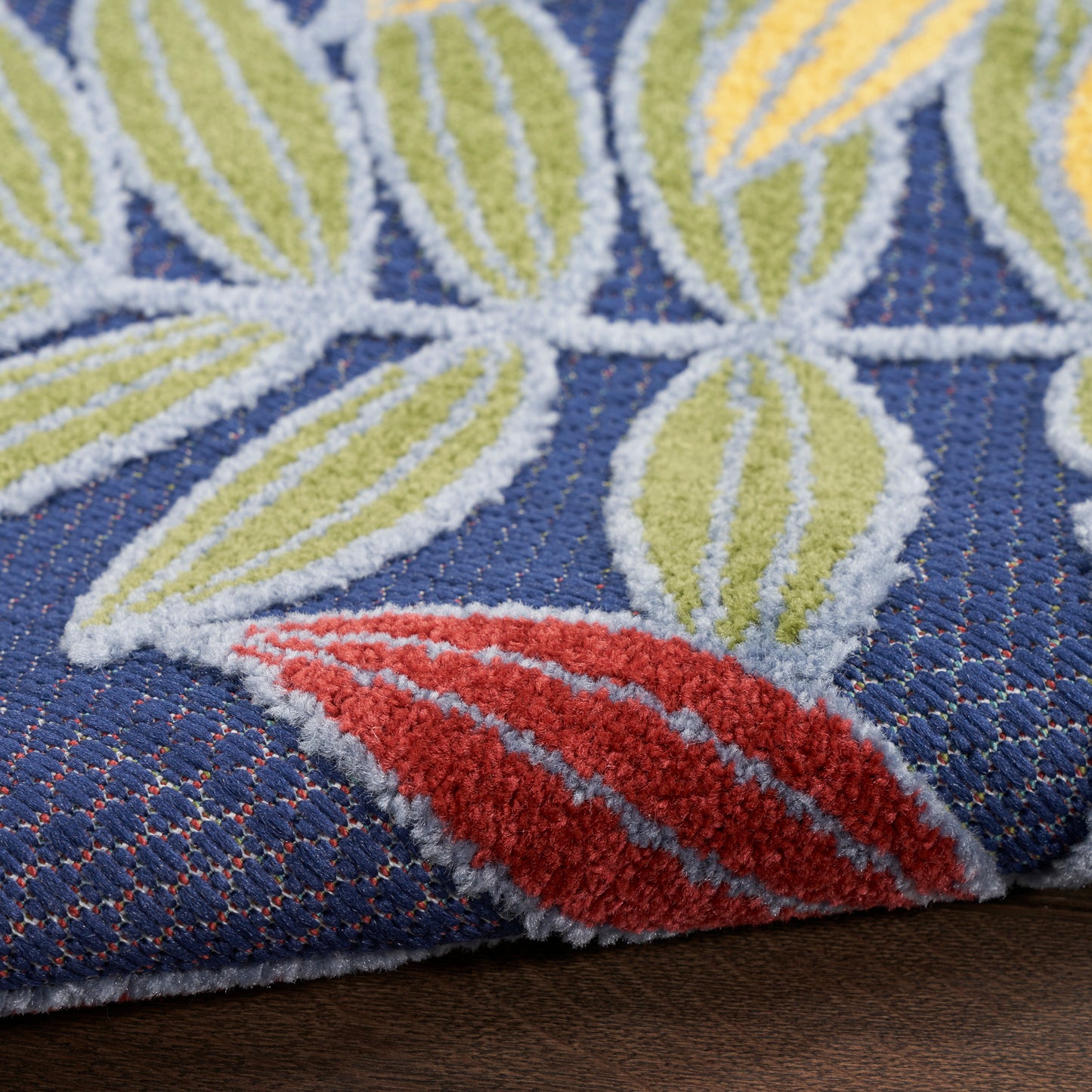 Close-up of blue tufted rug featuring white outlined lime-green leaves and a red leaf accent.
