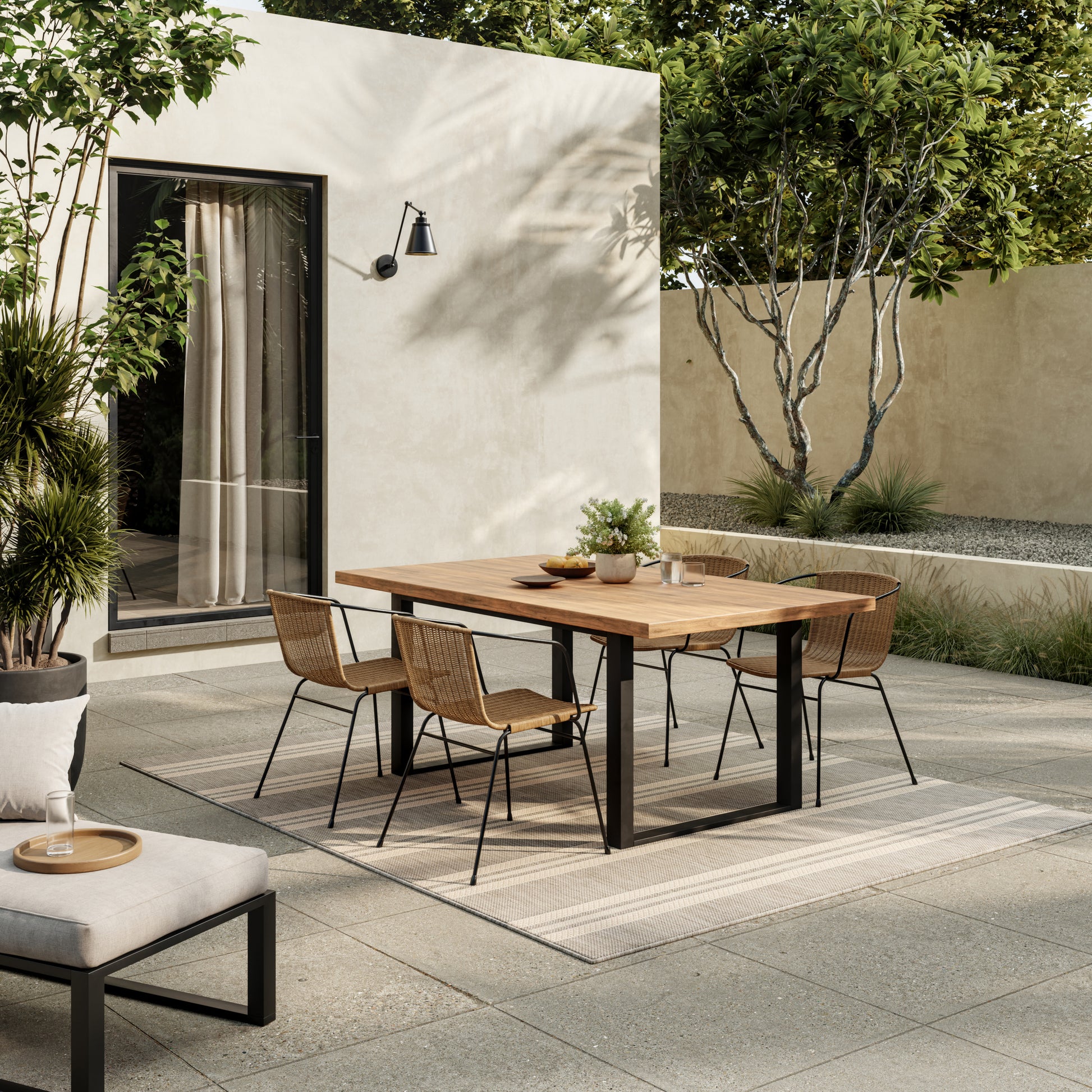 Modern outdoor dining set: rectangular wooden table with black metal legs and woven rattan chairs in a beige courtyard.