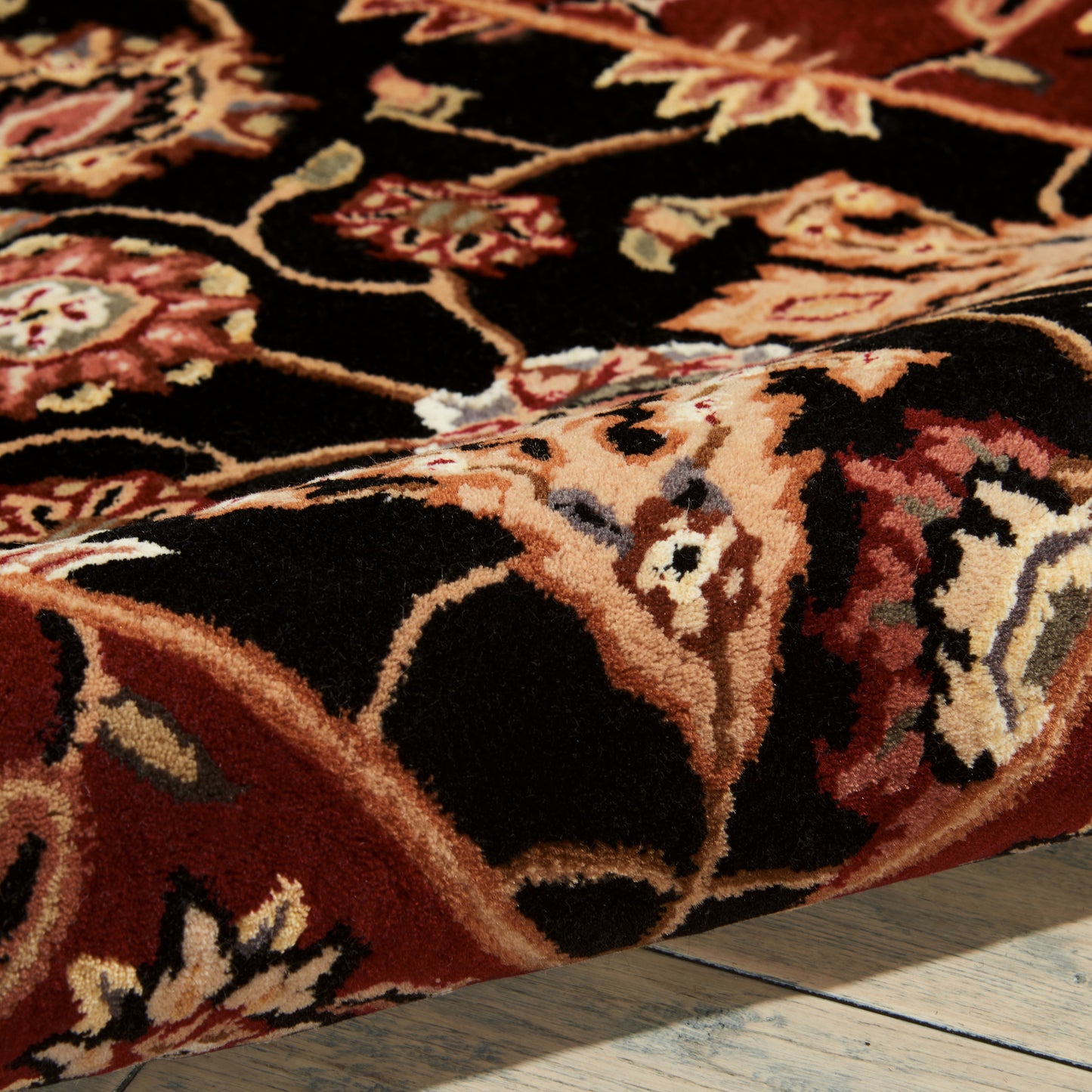 Oriental floral rug in black, red and beige with ornate border and thick pile on a wooden floor