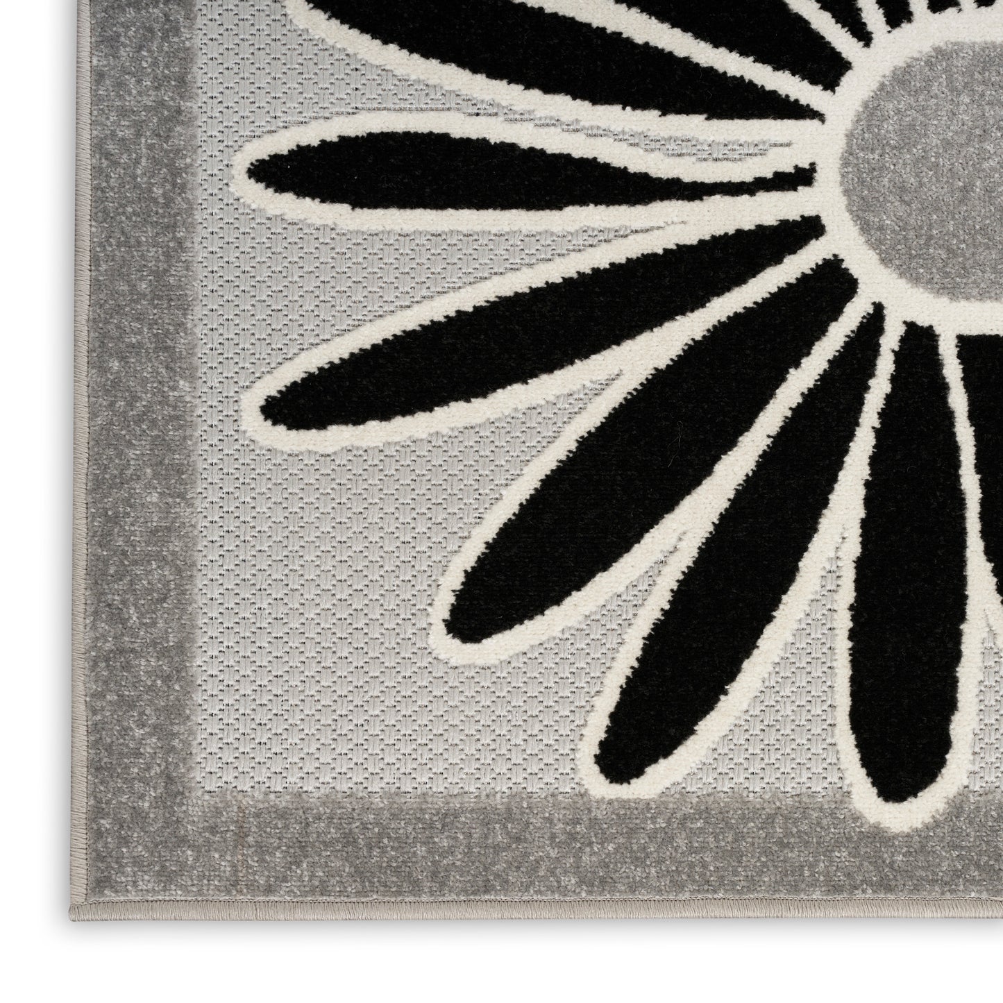 Close-up of a gray-bordered floral rug with a large black petal flower outlined in white on a light gray background