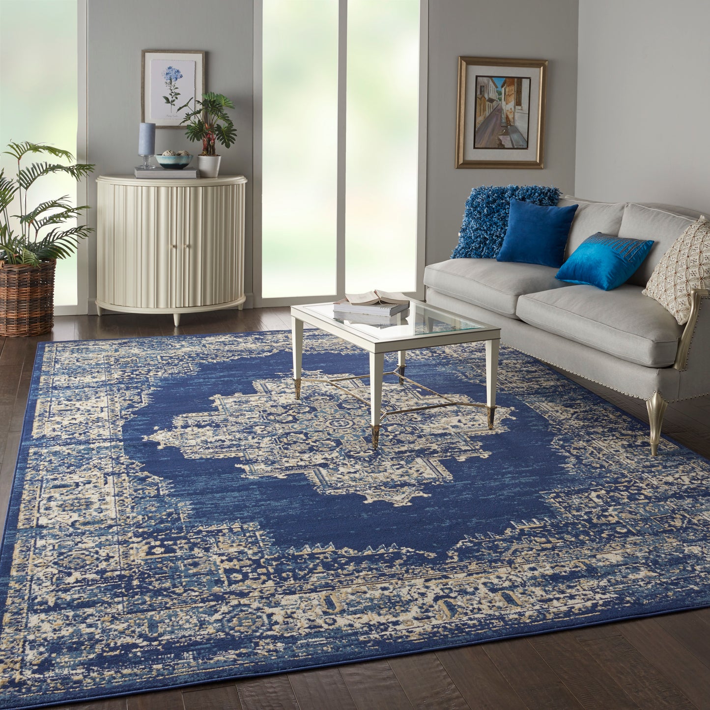 Blue and ivory distressed oriental rug in modern living room with cream sofa, glass coffee table, blue cushions and greenery.