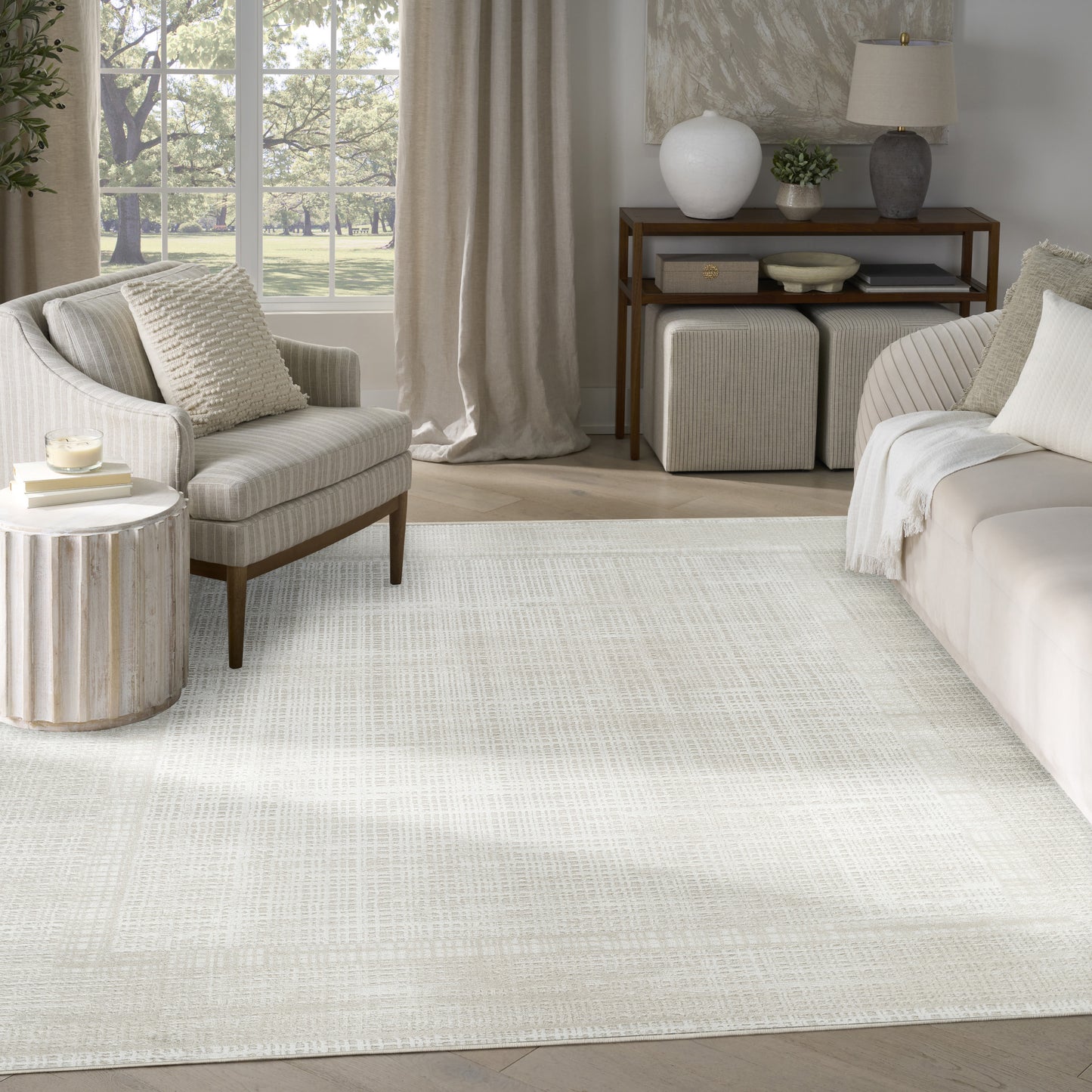 Neutral living room with cream textured rug, beige sofa and armchair, round ribbed side table, wooden console.