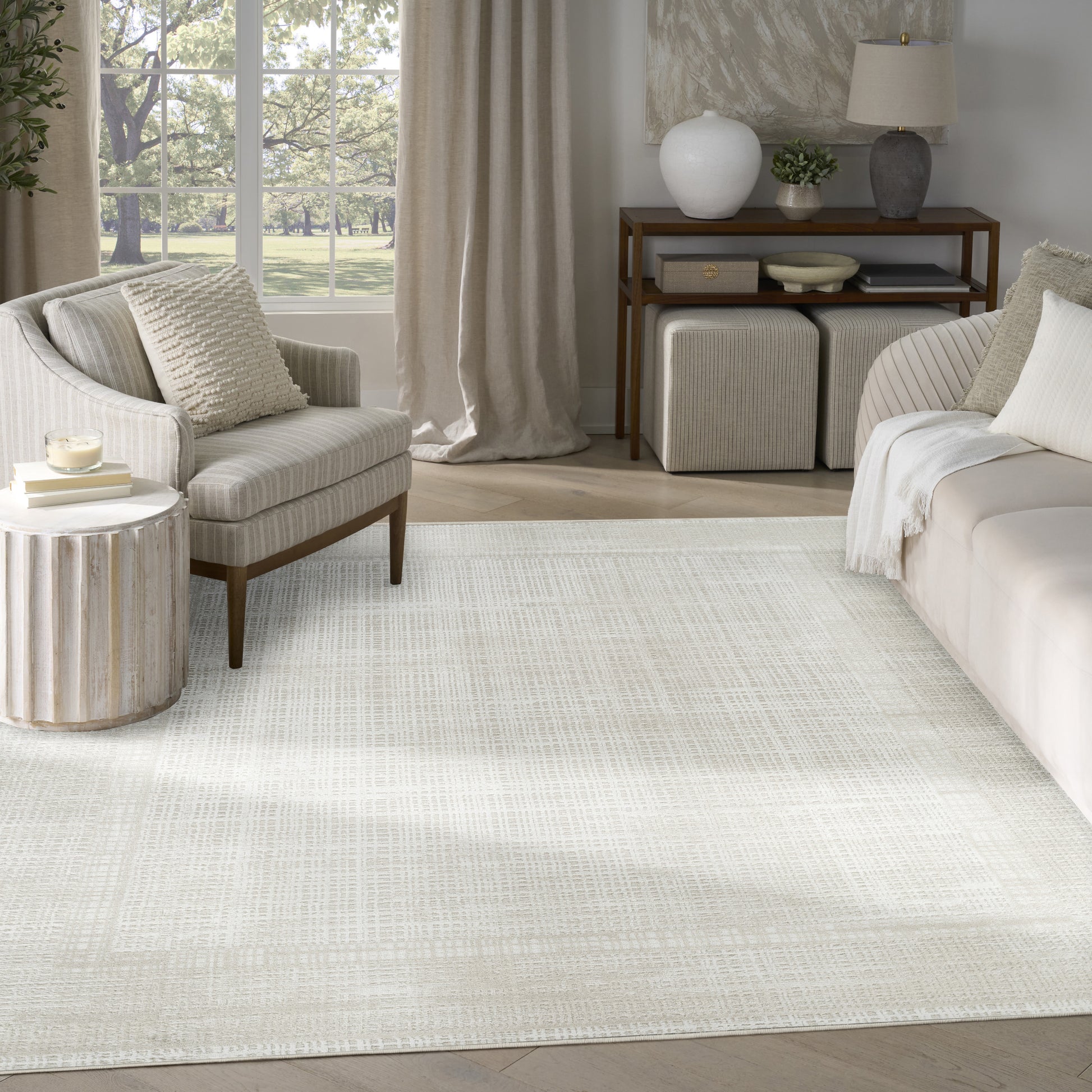 Neutral living room with cream textured rug, beige sofa and armchair, round ribbed side table, wooden console.