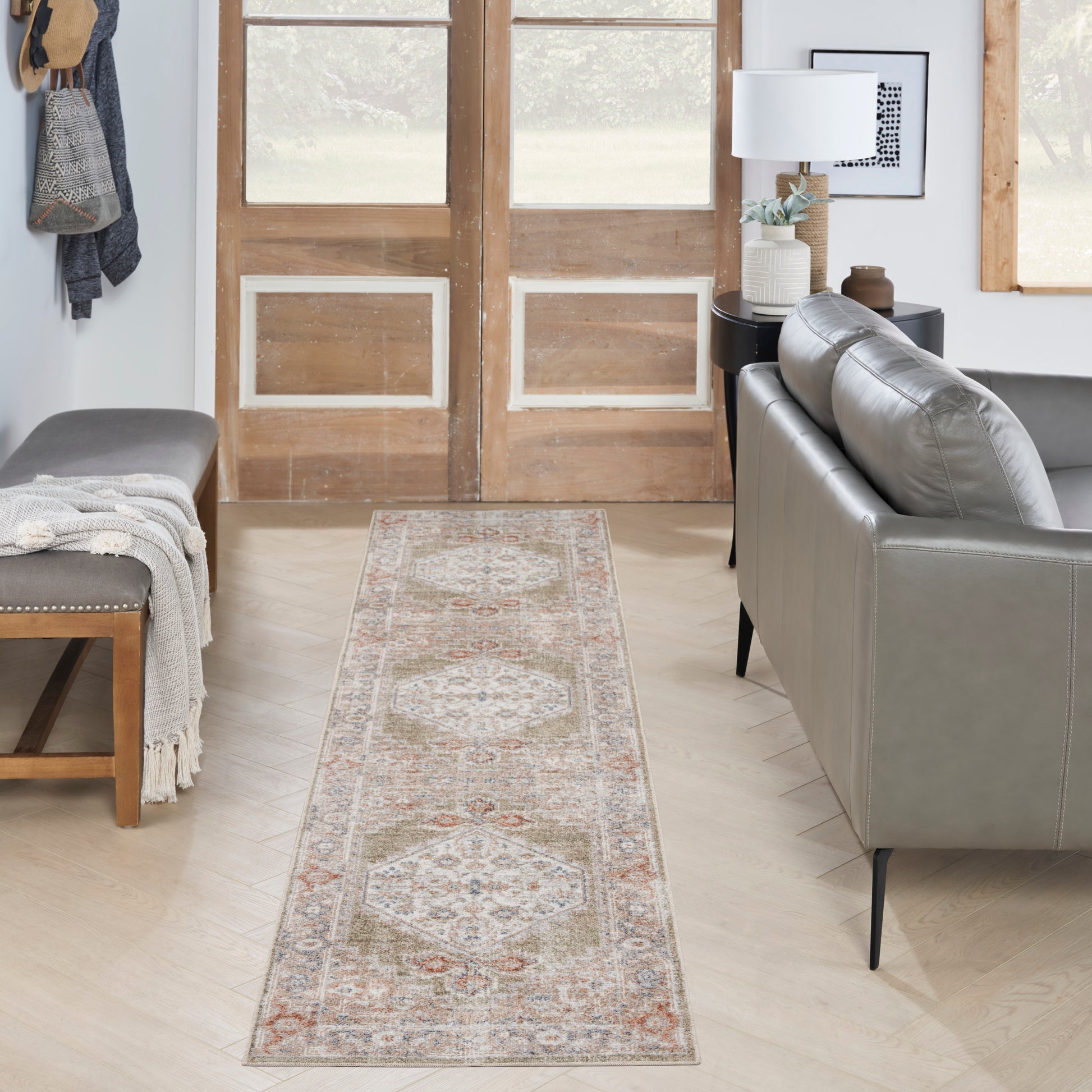 Long beige oriental runner rug with muted geometric medallions in blue and terracotta, laid along a light hardwood floor.