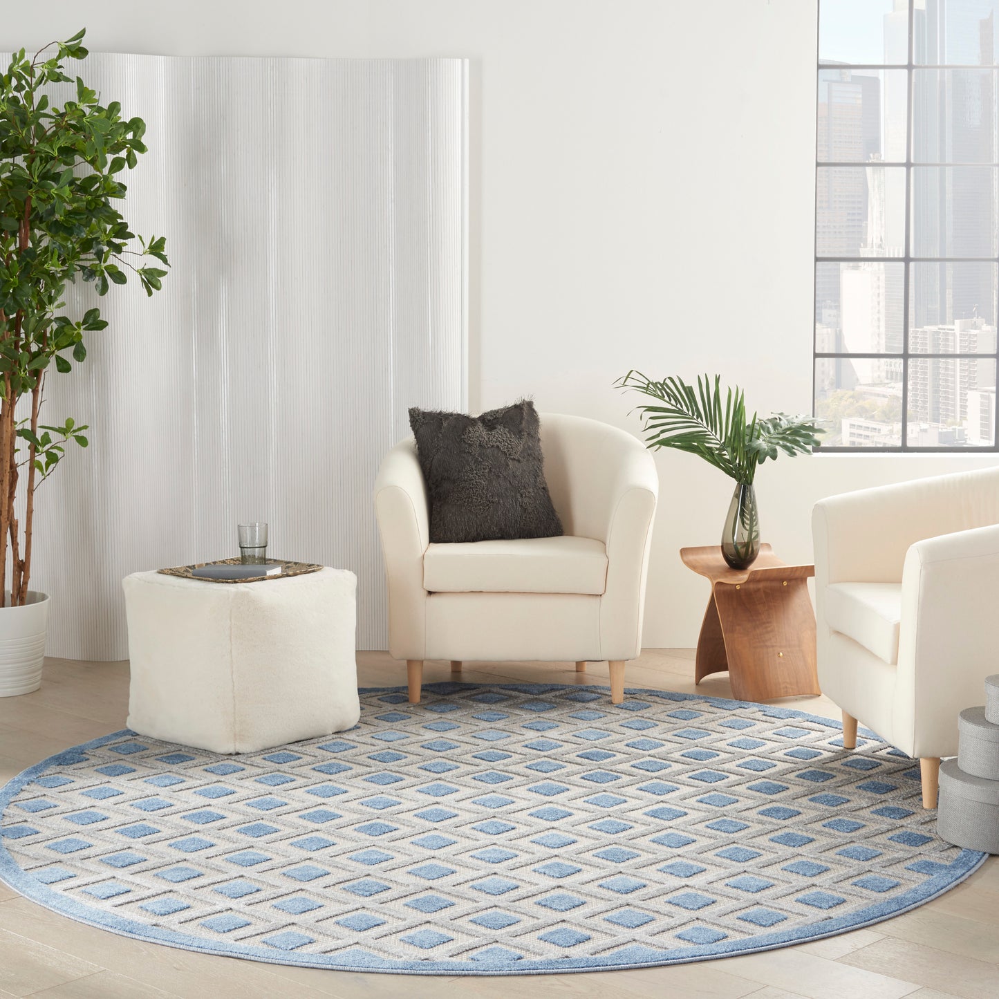 Round blue geometric rug under cream armchairs, white ottoman, wooden side table, and potted plants in a bright living room.