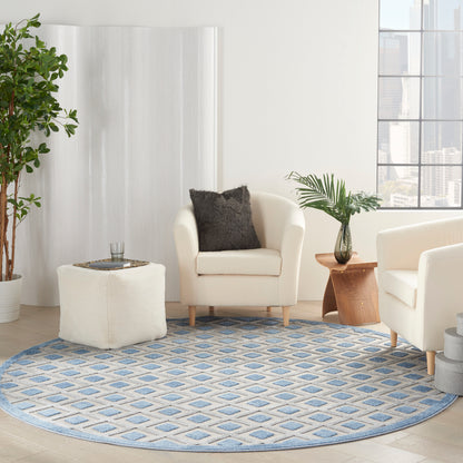 Round blue geometric rug under cream armchairs, white ottoman, wooden side table, and potted plants in a bright living room.