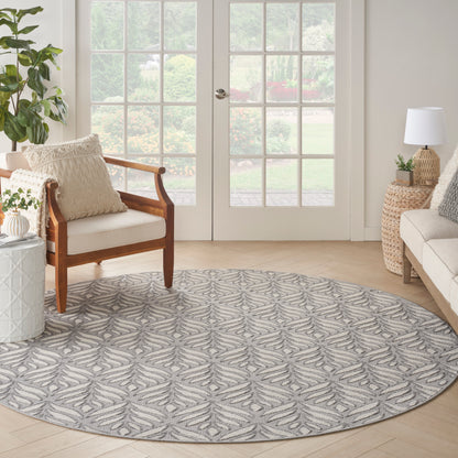 Round gray and ivory leaf-pattern area rug in a bright living room with wood chair, wicker side table, and French doors.