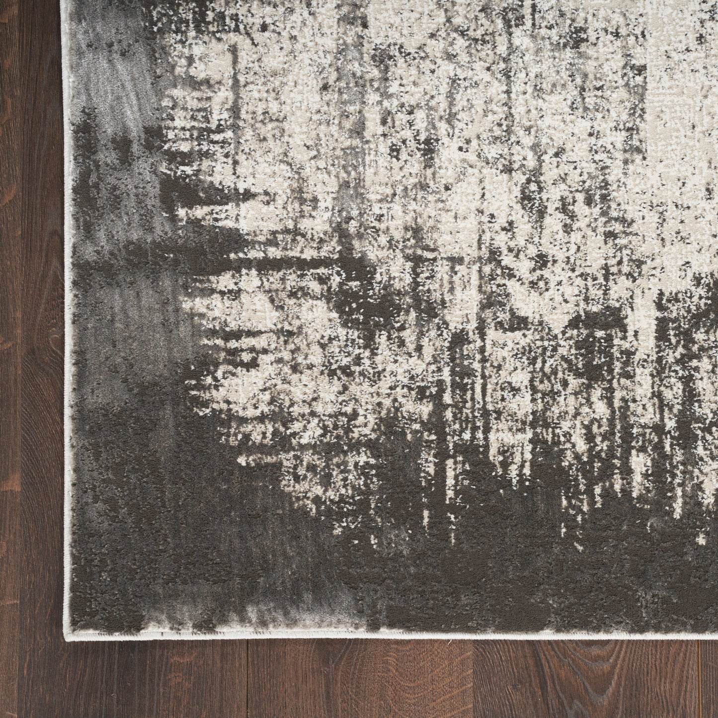 Rectangular area rug with abstract charcoal gray and ivory pattern, distressed look, light border, on dark wood floor.