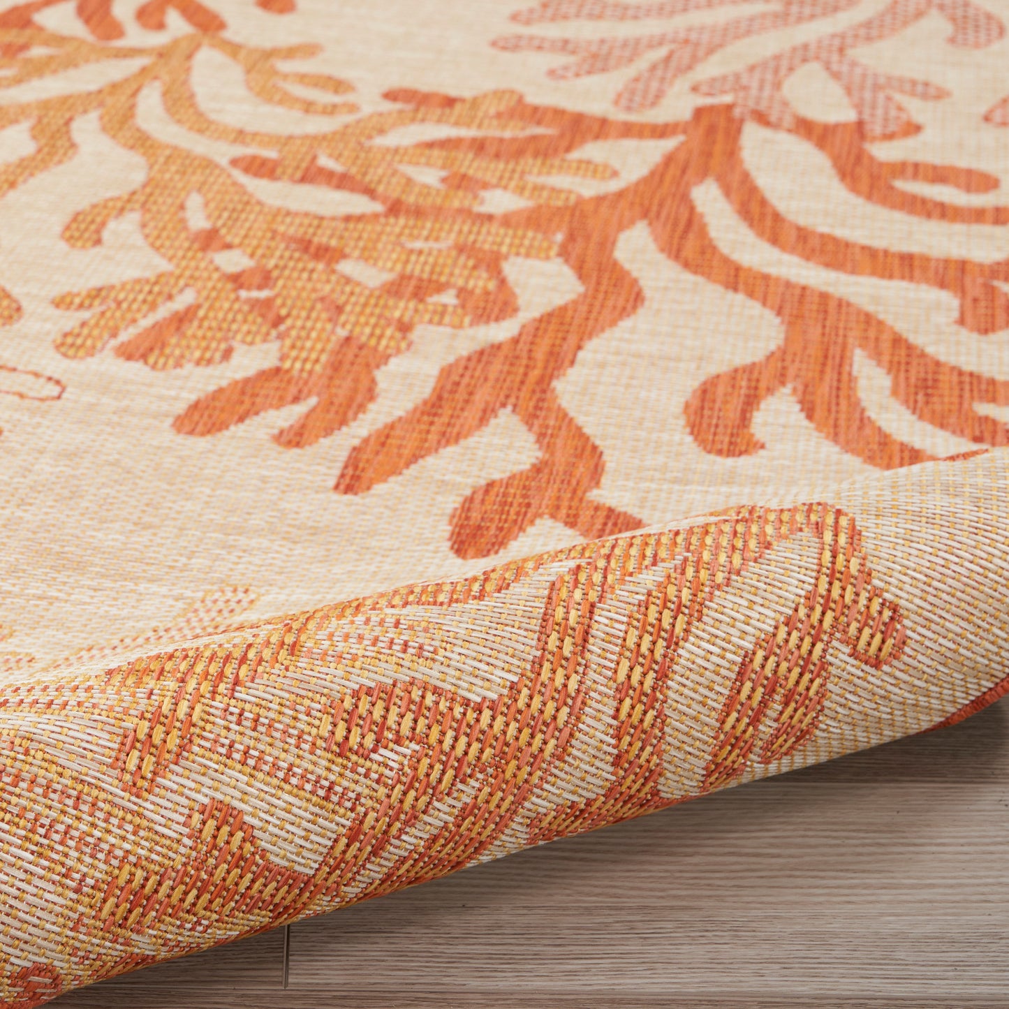 Beige woven rug with orange botanical motif, textured border, rolled corner, suitable for living room decor.
