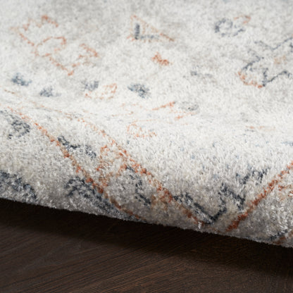 Close-up of plush cream rug with rust-orange and navy geometric patterns; thick pile, folded edge on dark wood floor.