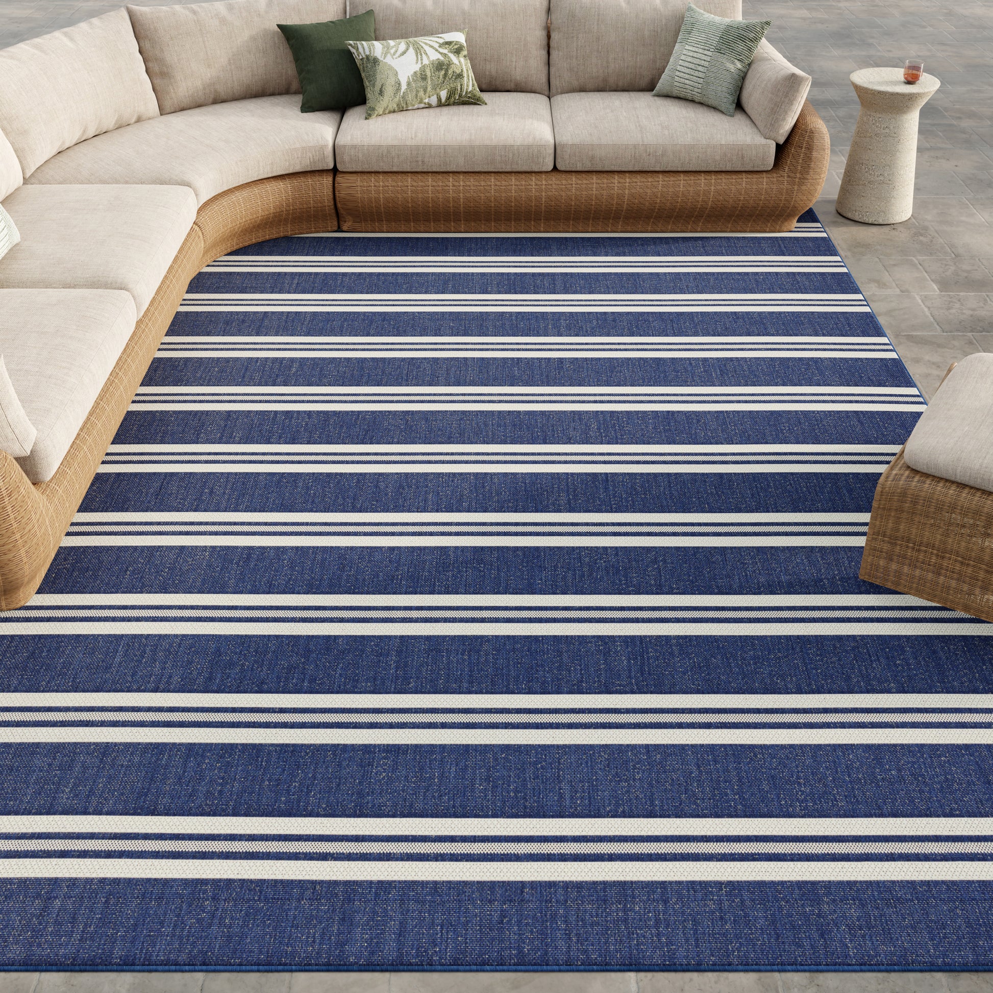 Blue striped woven area rug with white stripes under a beige curved wicker sectional in a coastal living room.