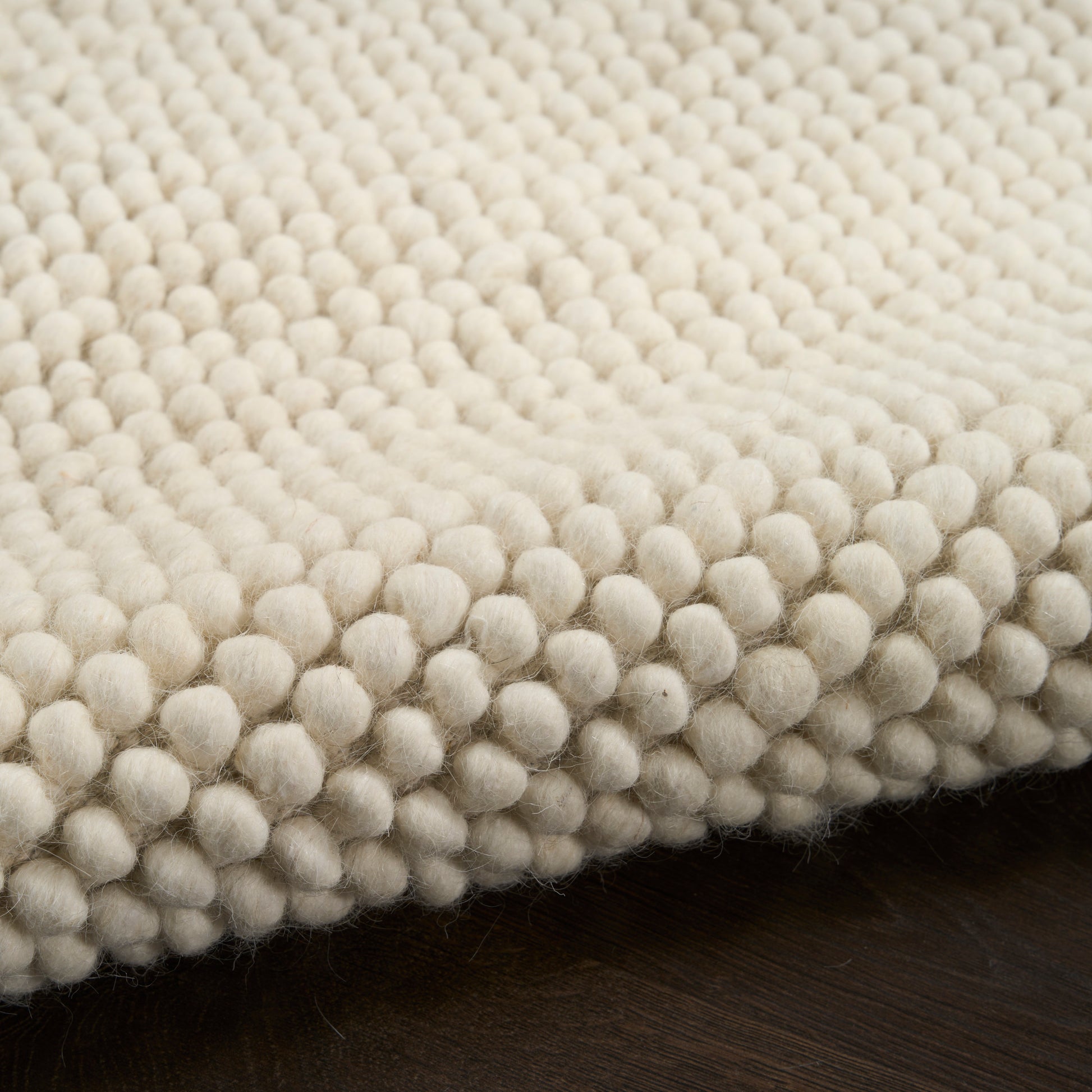 Cream wool rug with dense rounded pom-pom-like bumps and a soft textured pile on dark wood floor, 2' x 3