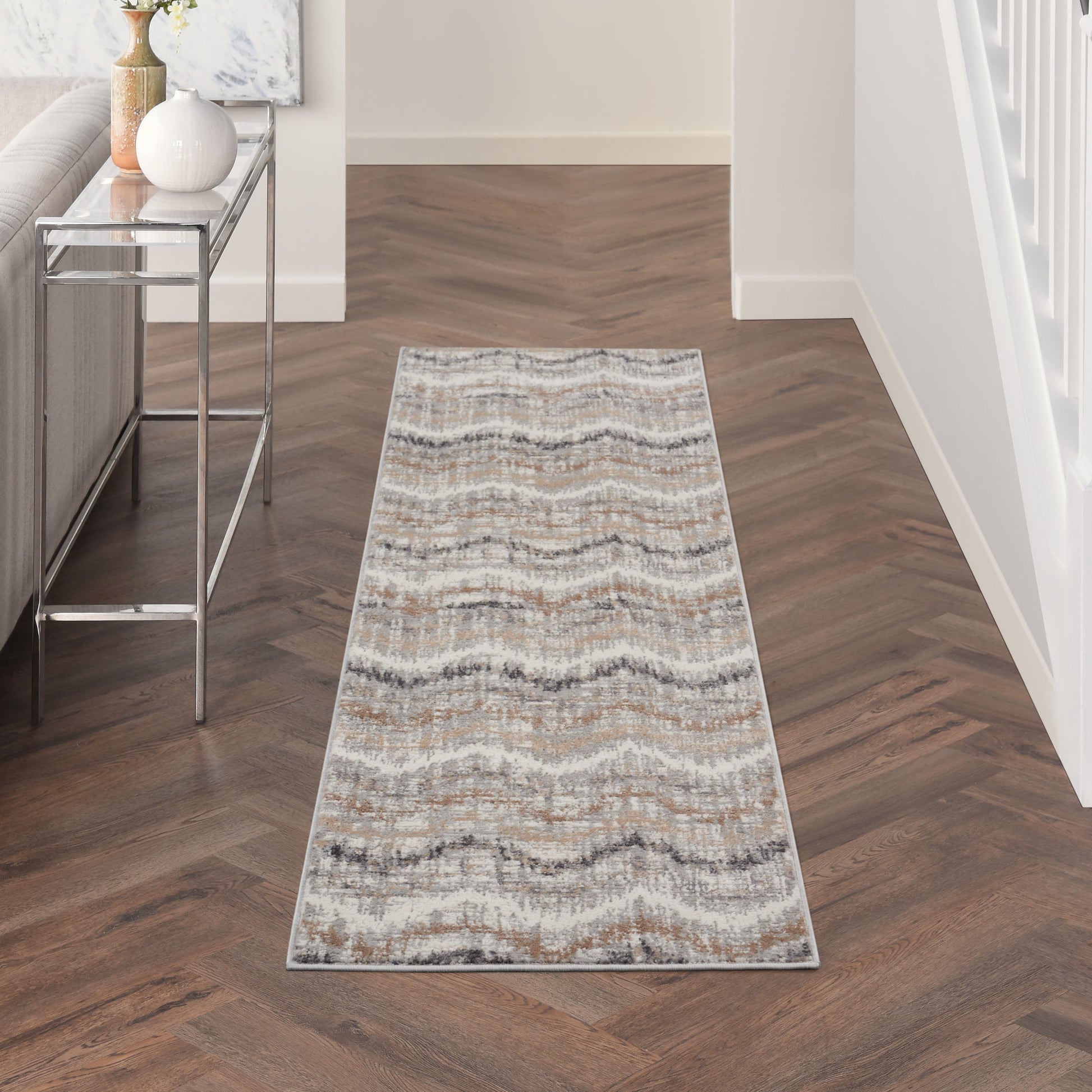 Long neutral-toned runner rug with wavy chevron pattern on wood hallway floor, beside a chrome console table.