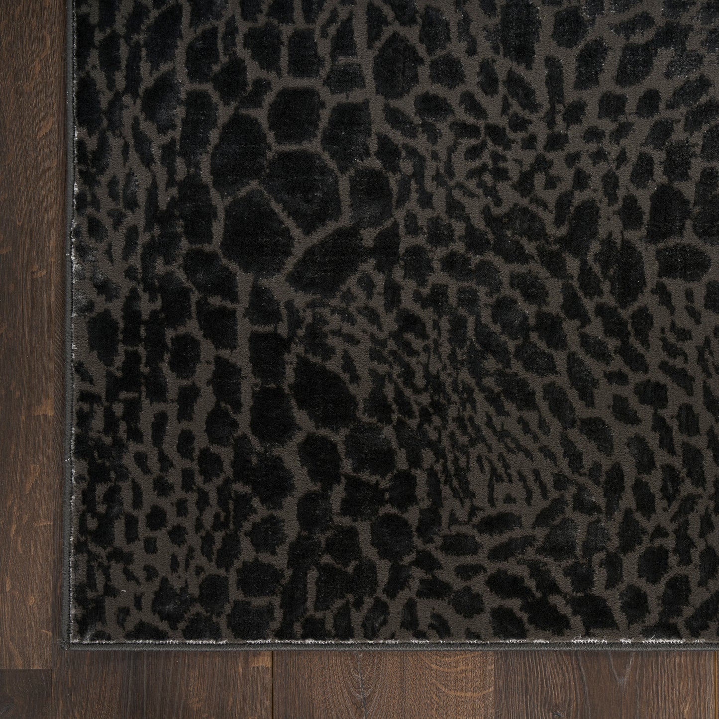 Rectangular black leopard-print rug on dark gray background; plush texture with wooden floor edge.