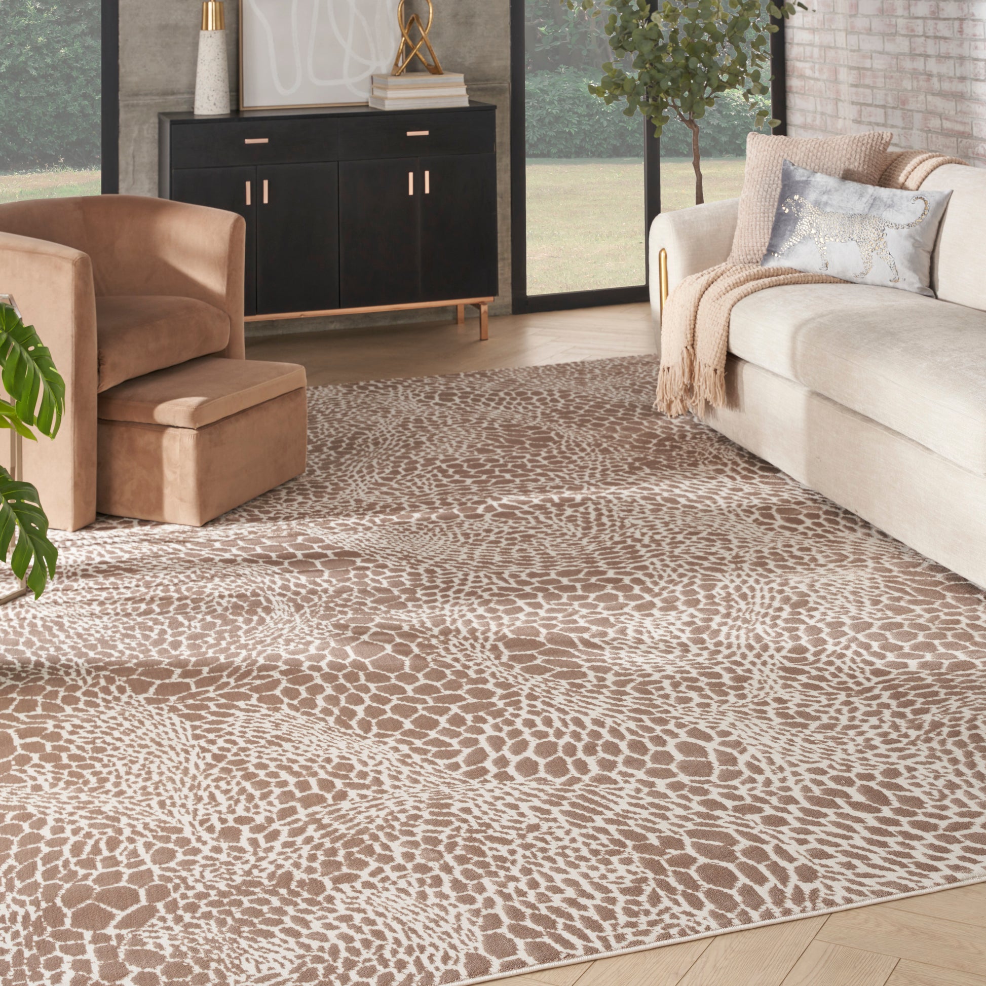 Neutral living room with tan and cream giraffe-pattern area rug, beige sofa, tan armchair, black cabinet and gold accents.