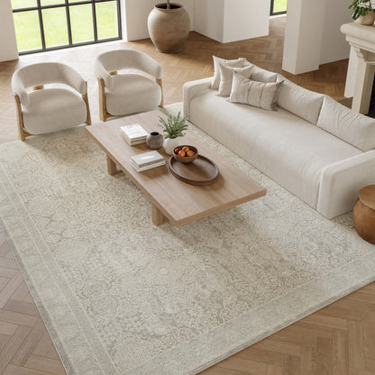 Beige patterned rug in a neutral living room with a cream sofa, two curved beige armchairs, and a light wood coffee table.