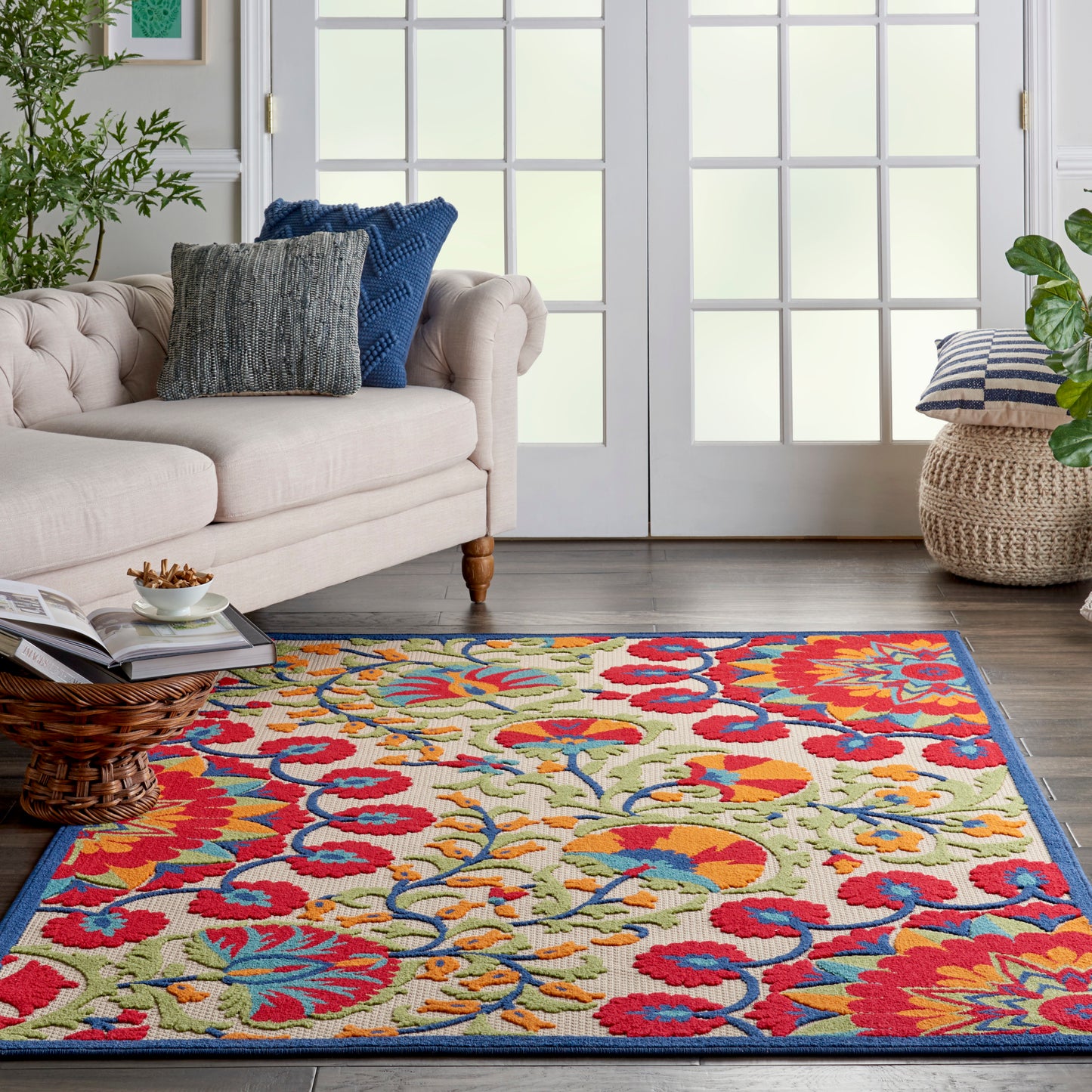 Multicolor floral area rug in a living room with beige tufted sofa, blue cushions, & wicker coffee table.