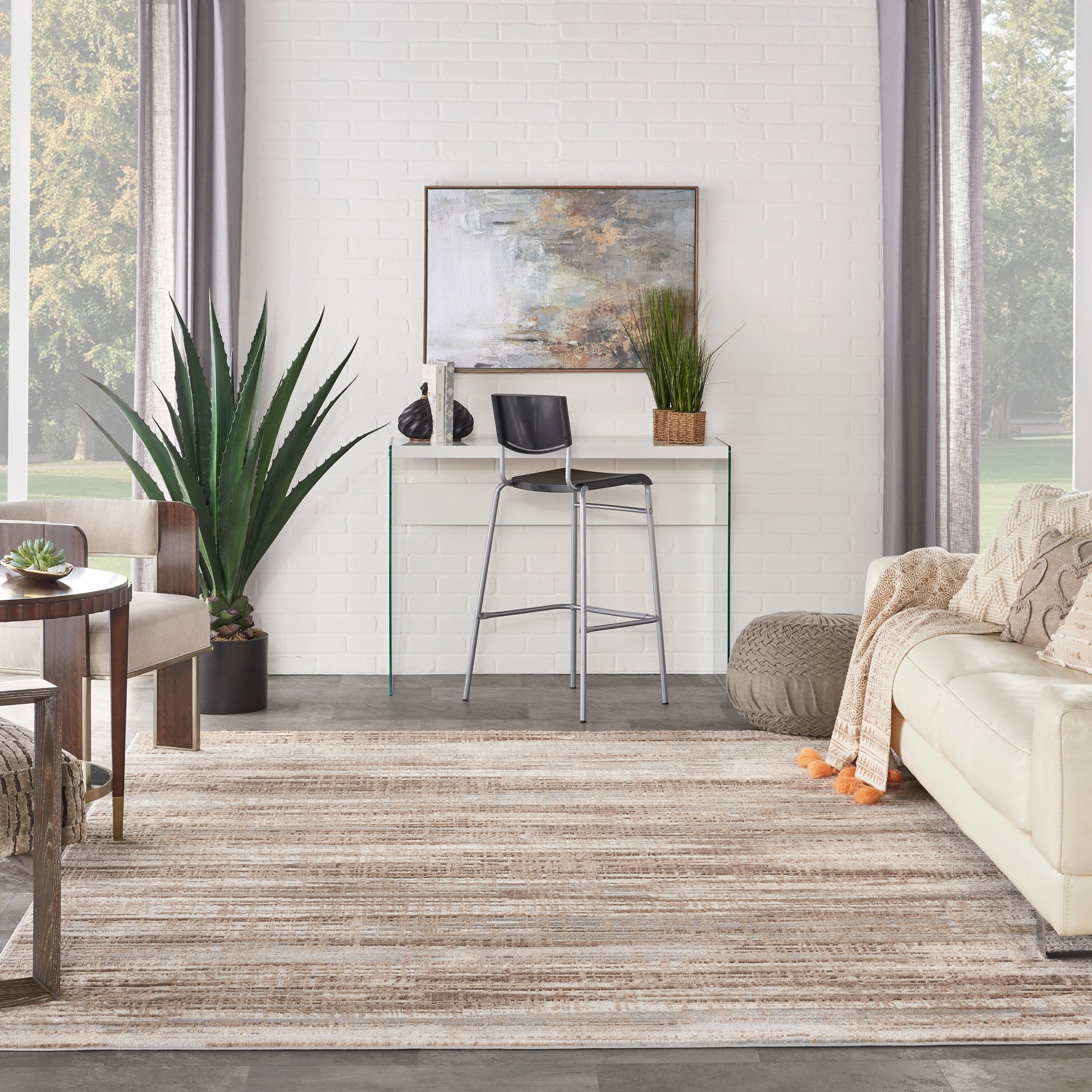Bright modern living room with white brick wall, glass-top console table, black bar stool, plants, beige sofa, striped rug.