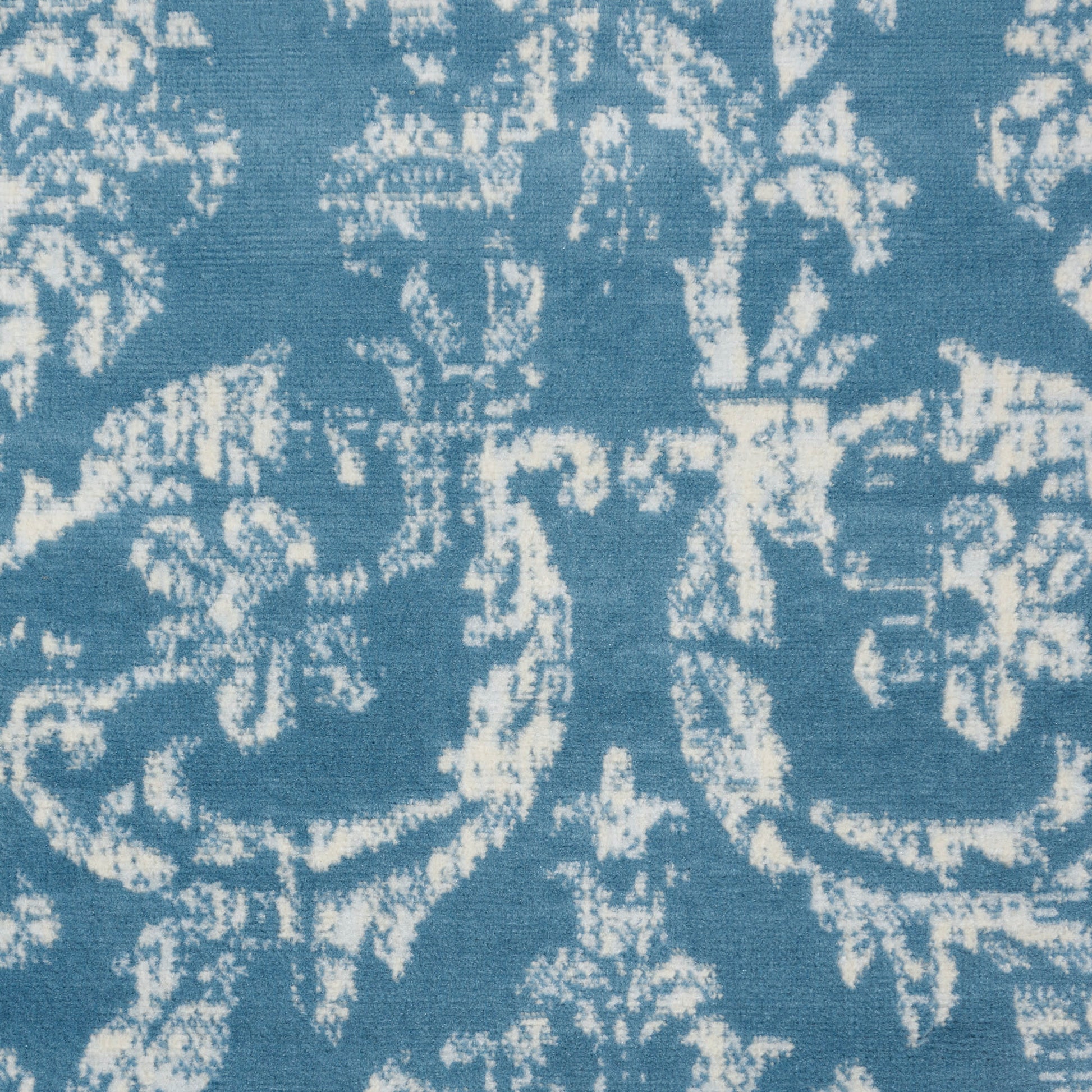 Blue fabric with a white distressed damask floral pattern, jacquard-style upholstery textile.