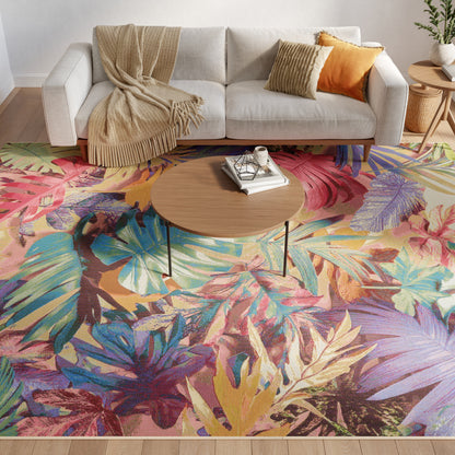 Round wooden coffee table with metal legs on a vivid tropical leaf rug, beige sofa with throw blanket and orange pillows.