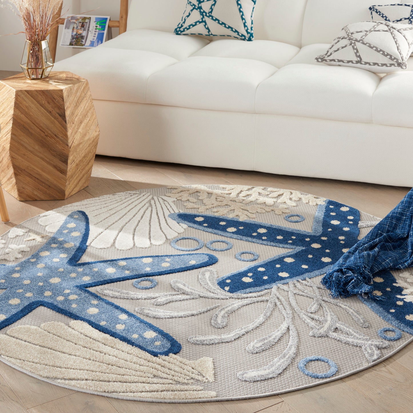 Round coastal rug with blue starfish motifs on cream background; soft plush pile.