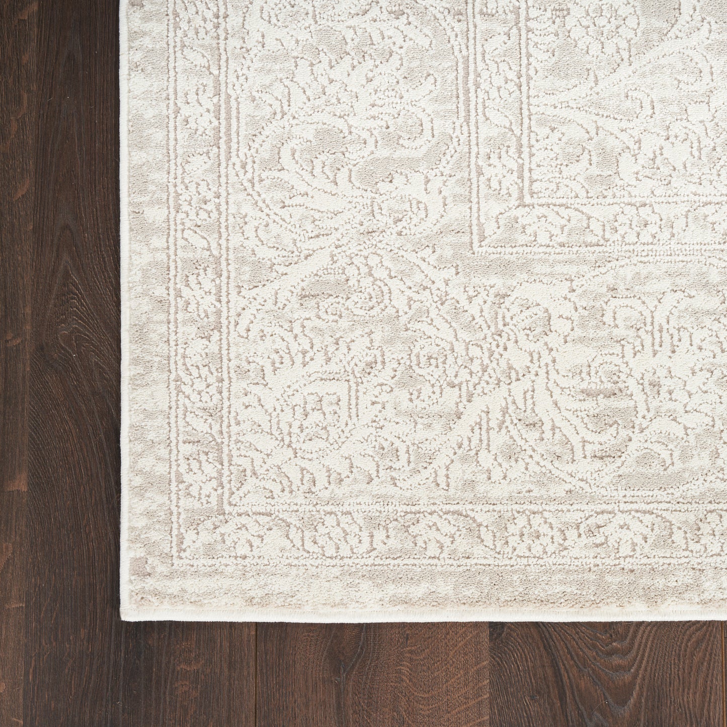 Cream beige rug with ornate damask floral border on dark wood floor.