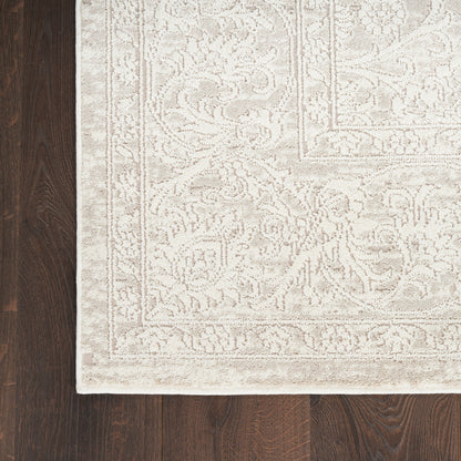 Cream beige rug with ornate damask floral border on dark wood floor.