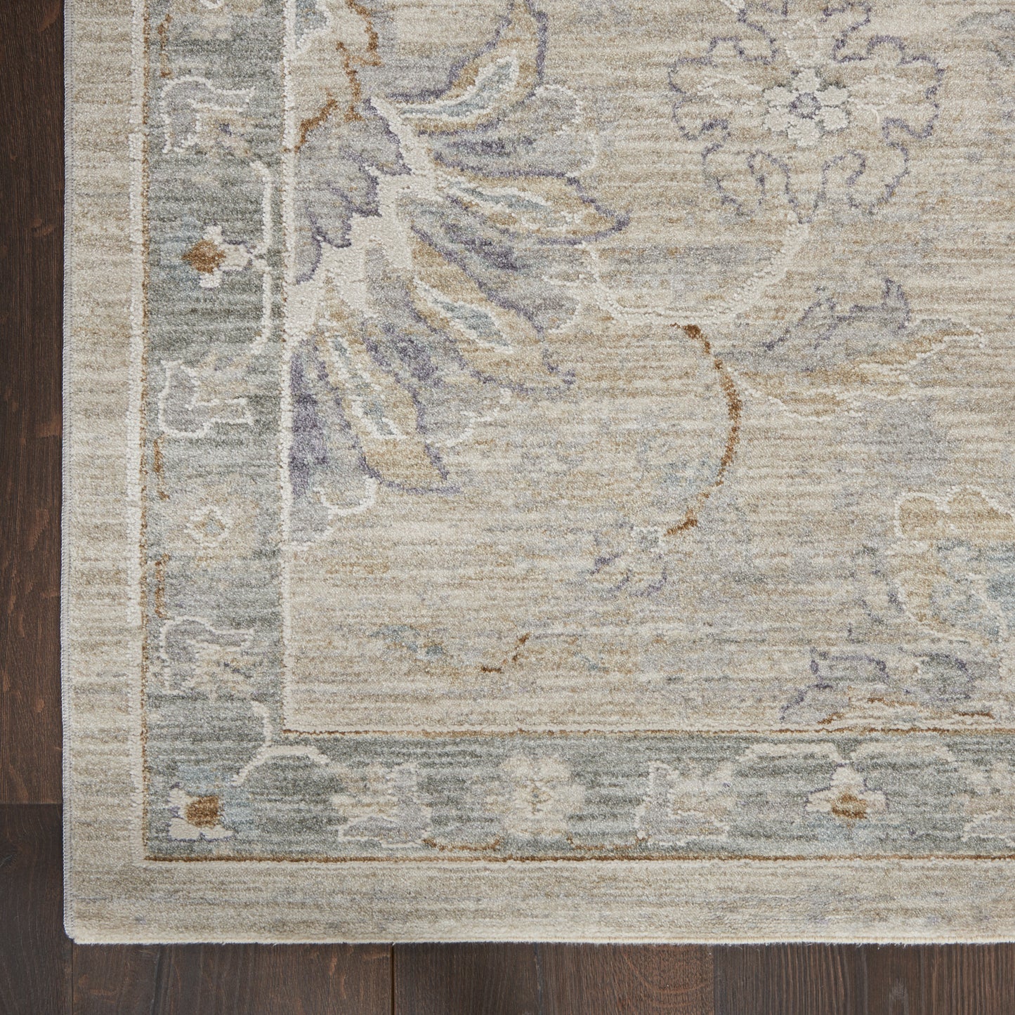 Muted beige rug with blue-gray floral motif and pale border on dark wooden floor.