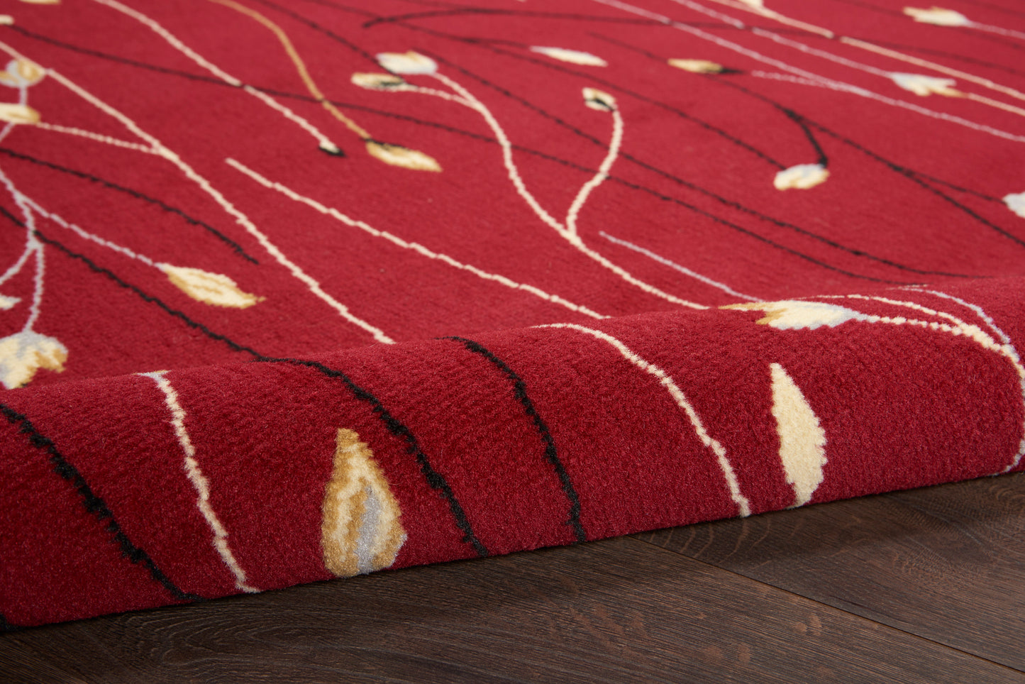Red rug with cream and black abstract lines and pale yellow accents; rolled corner on dark wood floor.