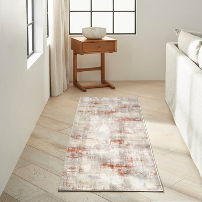 Abstract runner rug in cream, gray and rust tones on light wood floor beside a wooden side table and cream sofa.