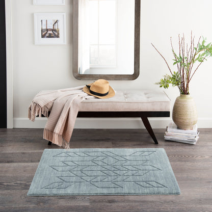 Beige tufted bench with dark wood legs, beige throw and straw hat, mirrored wall, vase with branches, geometric rug.