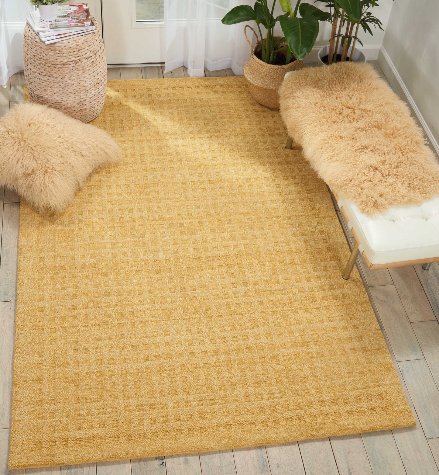 Rectangular golden-yellow woven rug with subtle check, beige faux-fur cushions, light wood floor and potted plants.