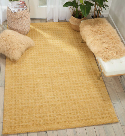 Rectangular golden-yellow woven rug with subtle check, beige faux-fur cushions, light wood floor and potted plants.