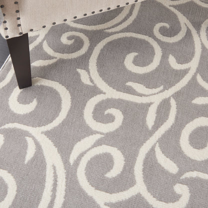 Gray rug with white ornate swirl pattern and a dark wooden chair leg resting on it.