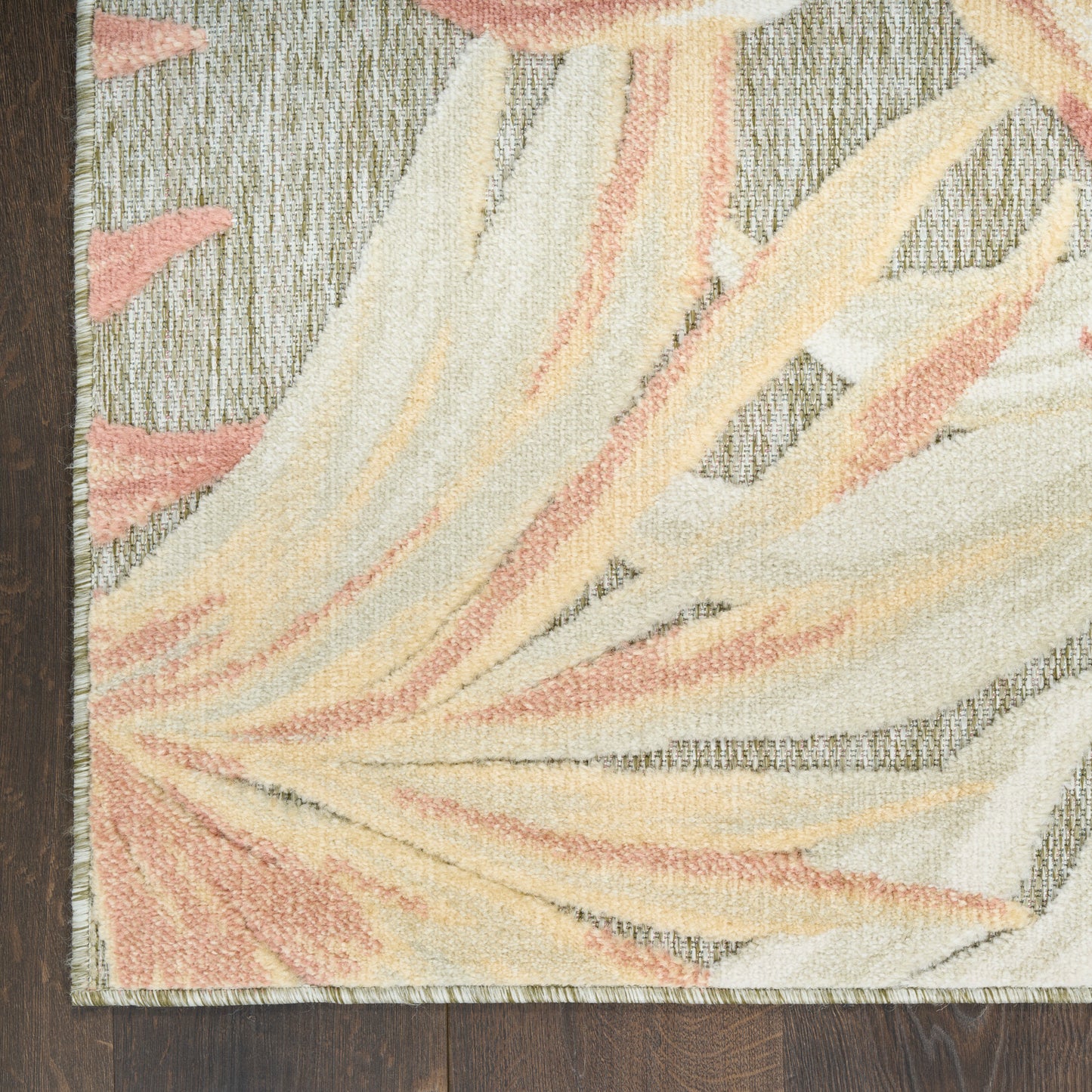 Pastel palm-leaf rug with cream, peach and pale yellow tones, textured loop pile on dark wood floor.