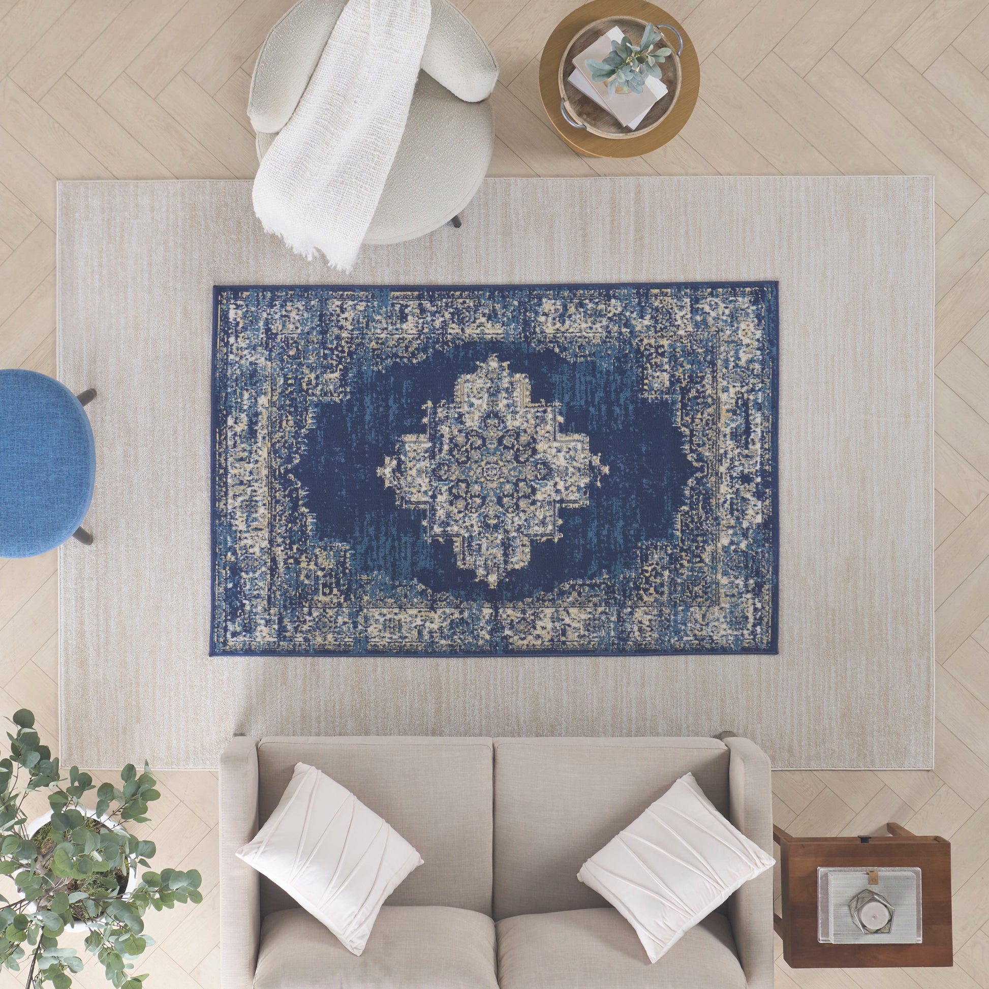 Blue distressed oriental rug with central medallion laid over a beige area rug in a modern neutral living room.
