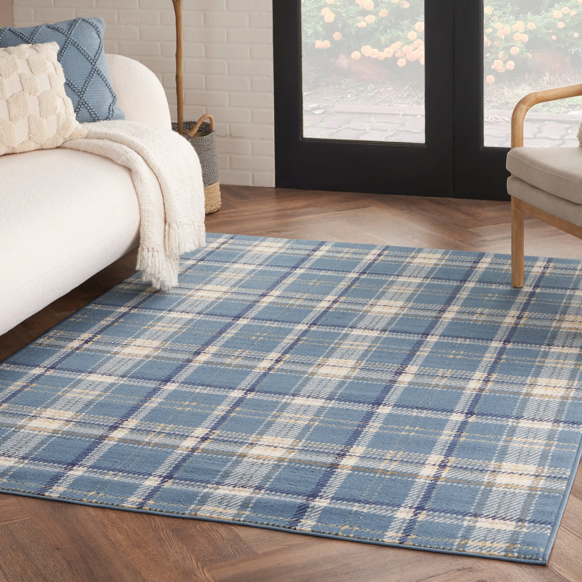 Blue plaid area rug with yellow and cream accents on hardwood floor beside cream sofa and woven throw in cozy living room.