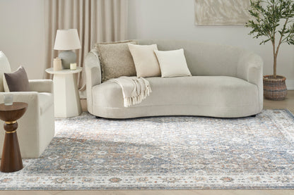 8' x 10' blue-gray patterned rug in a calm living room, with a light beige curved sofa, neutral cushions, and a throw.