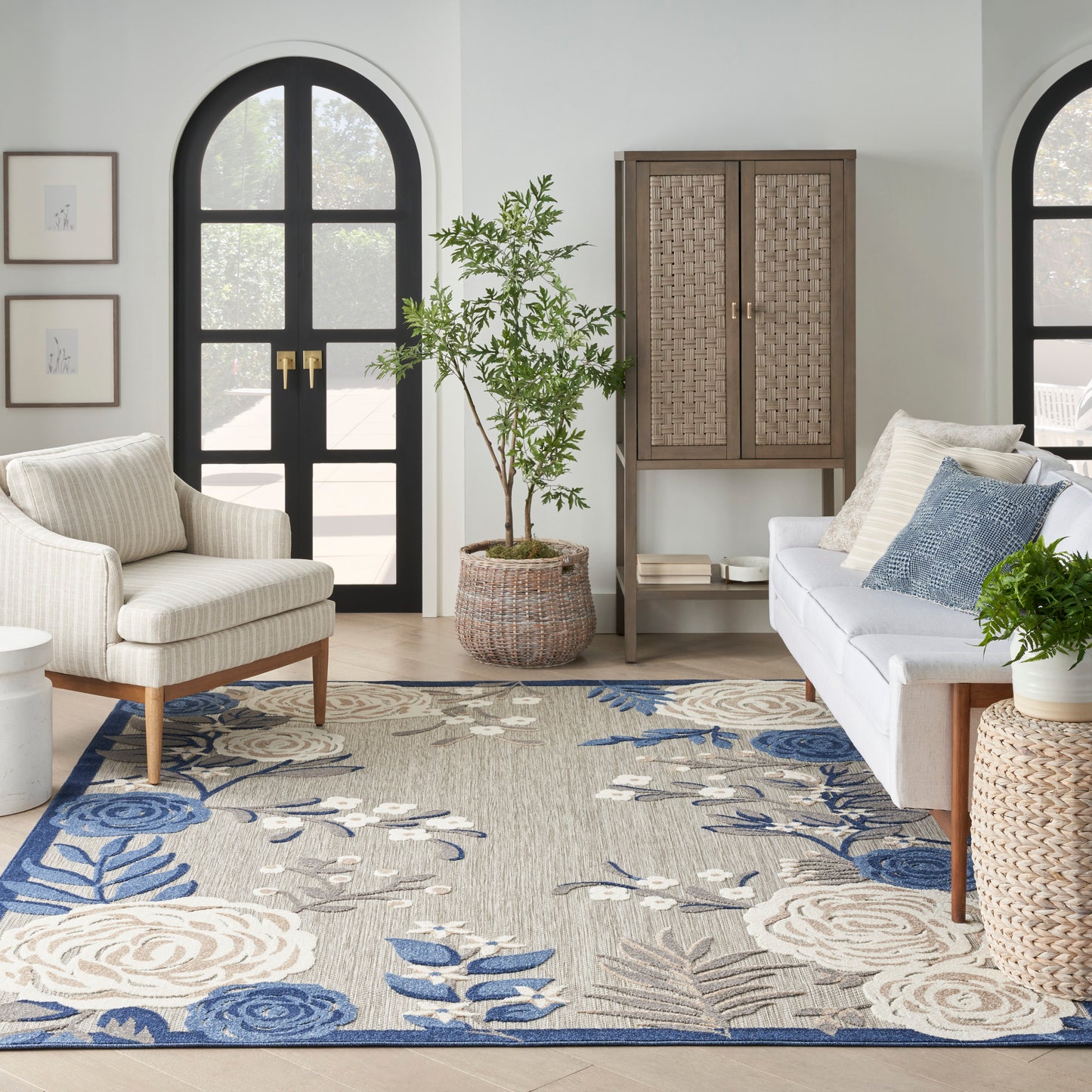 Blue floral contemporary rug (5' x 8') in a living room with beige armchairs, gray sofa, woven cabinet, arched black doors, and a potted plant.